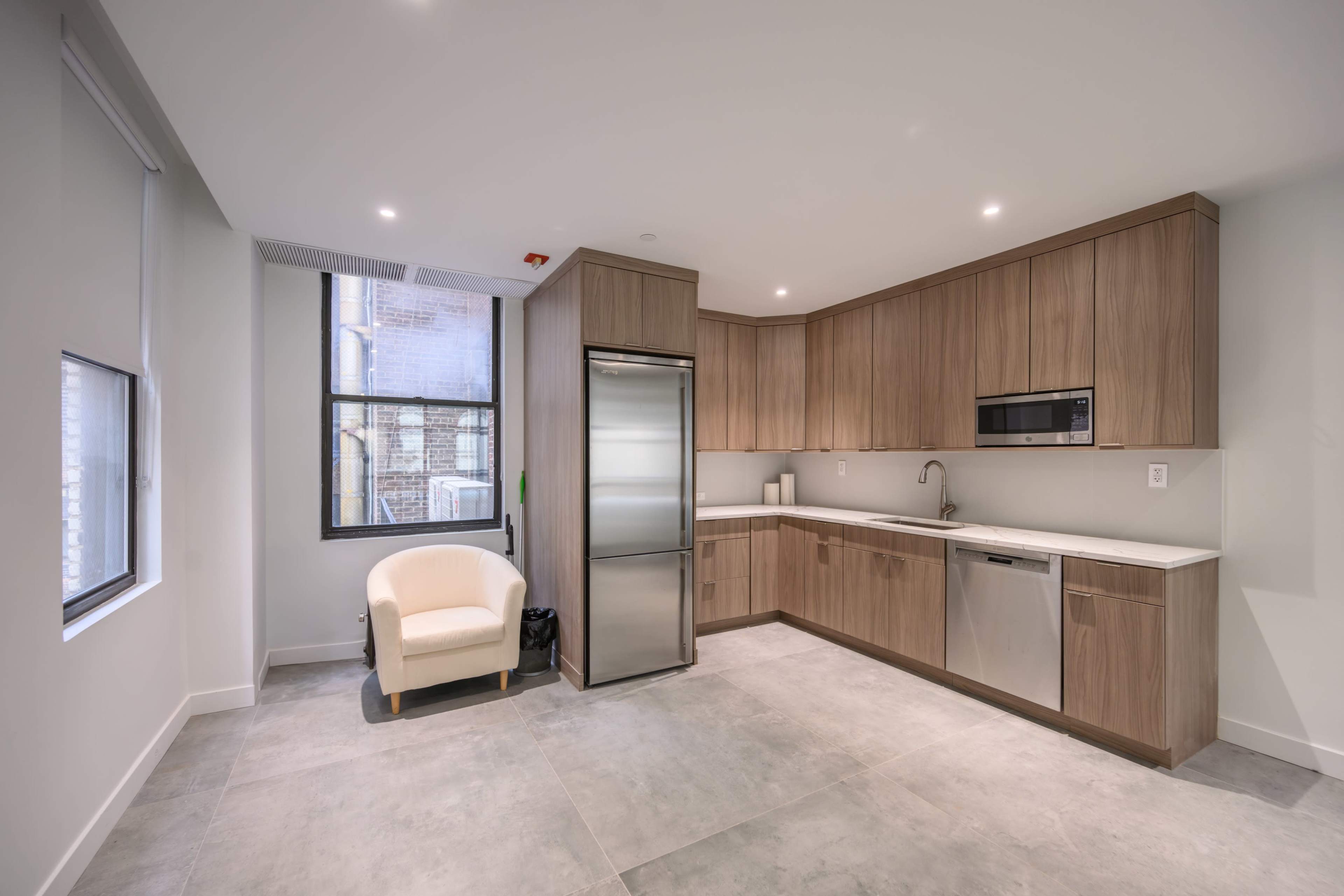 The image shows a modern kitchen with wooden cabinetry, stainless steel appliances, and a beige armchair in a corner.