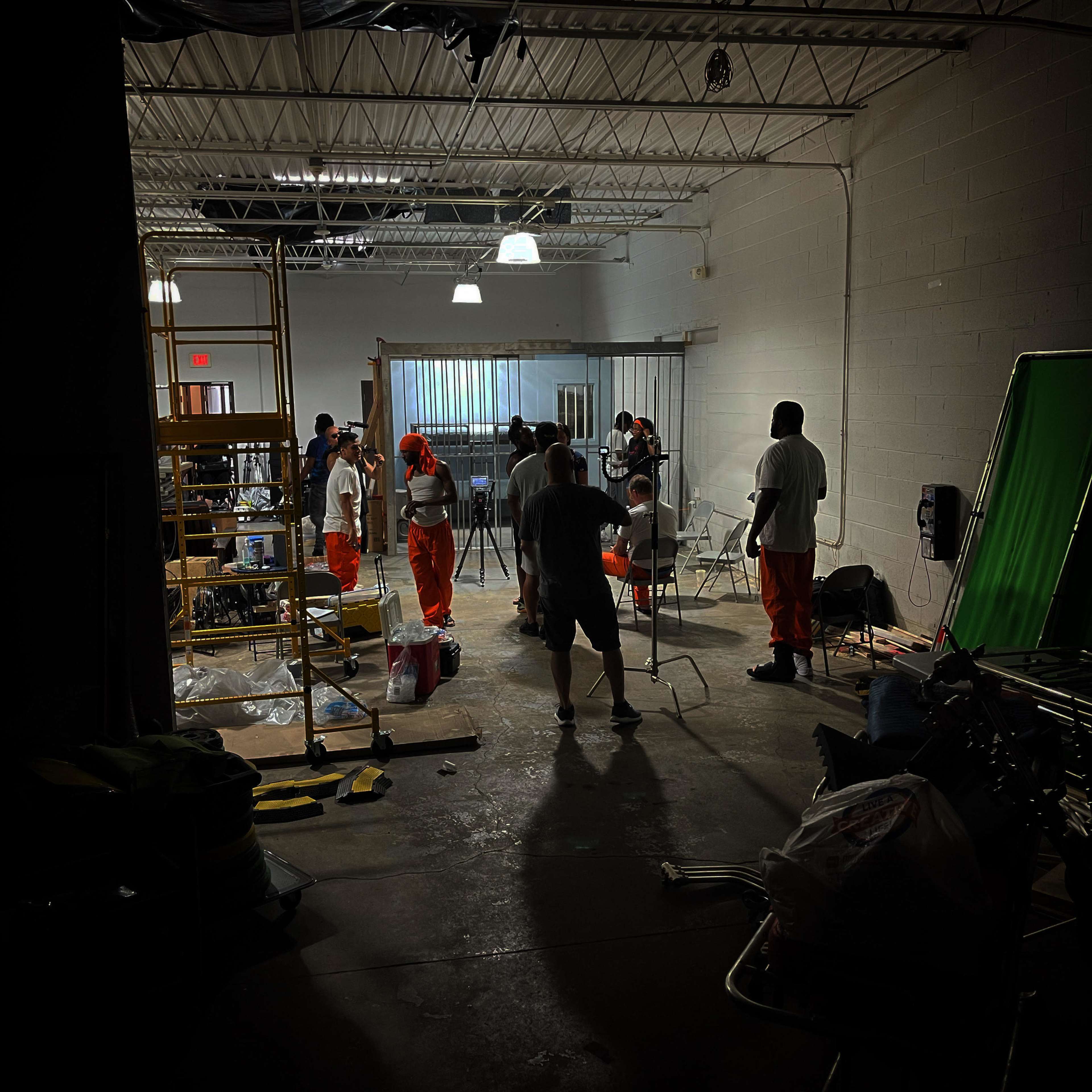 A group of people dressed in orange clothing is gathered in a warehouse-like space with various equipment and lighting setups.