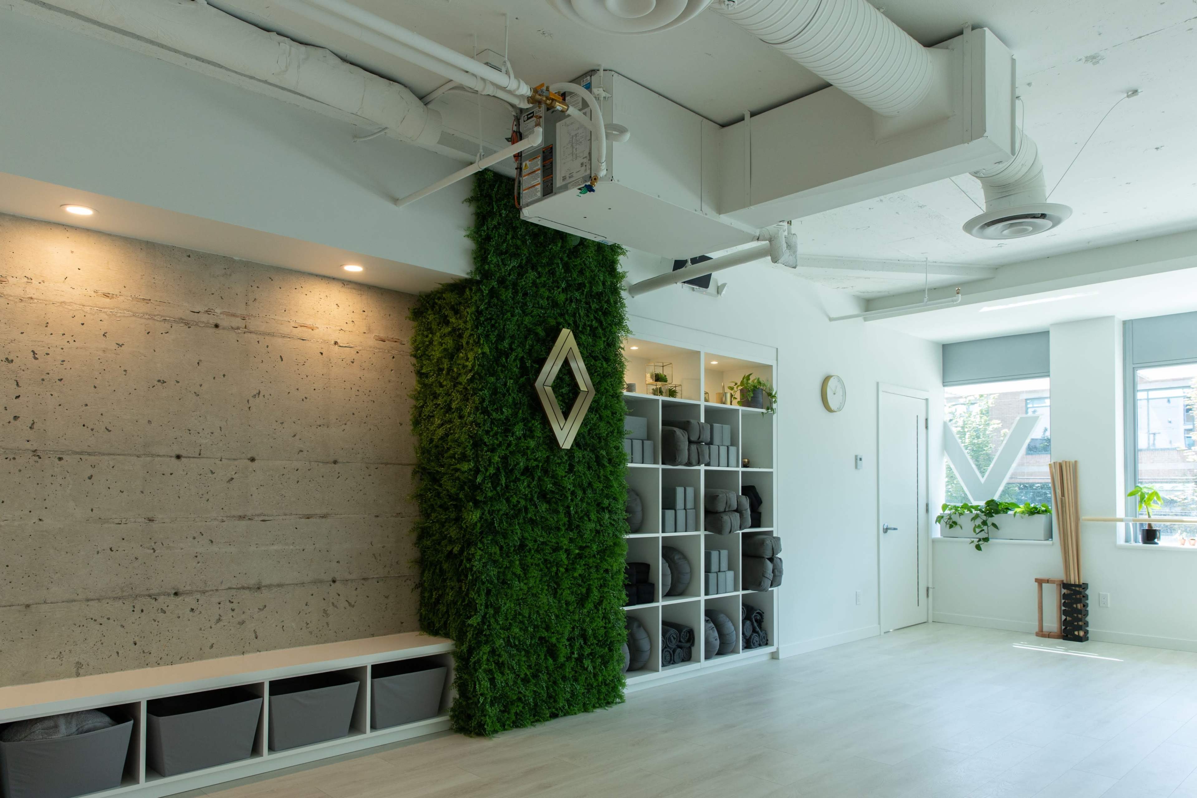 A modern, minimalistic interior featuring a green moss wall, gray storage bins, and large windows with plants.