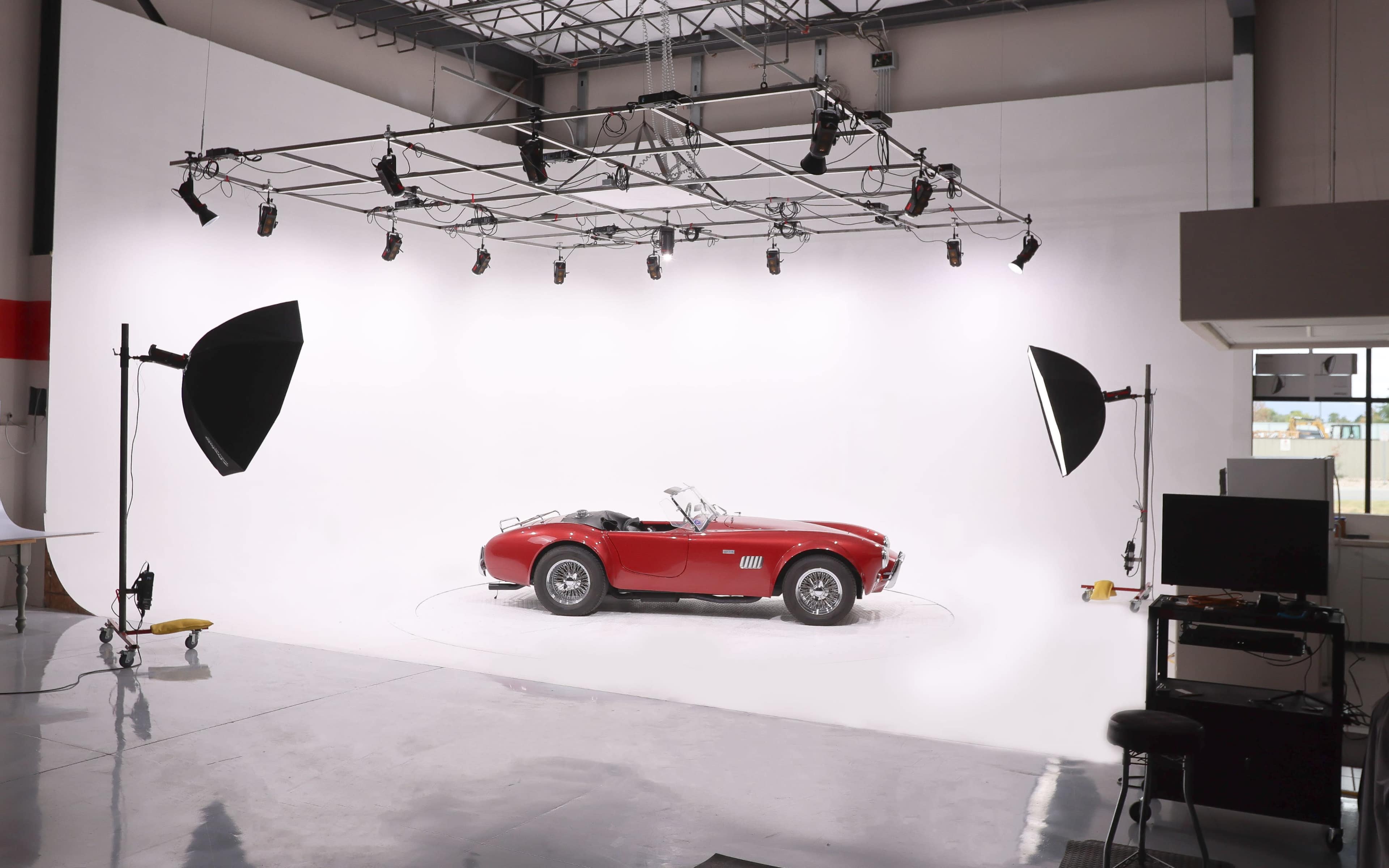 A red convertible sports car is positioned in a photography studio with bright lighting and a white backdrop.