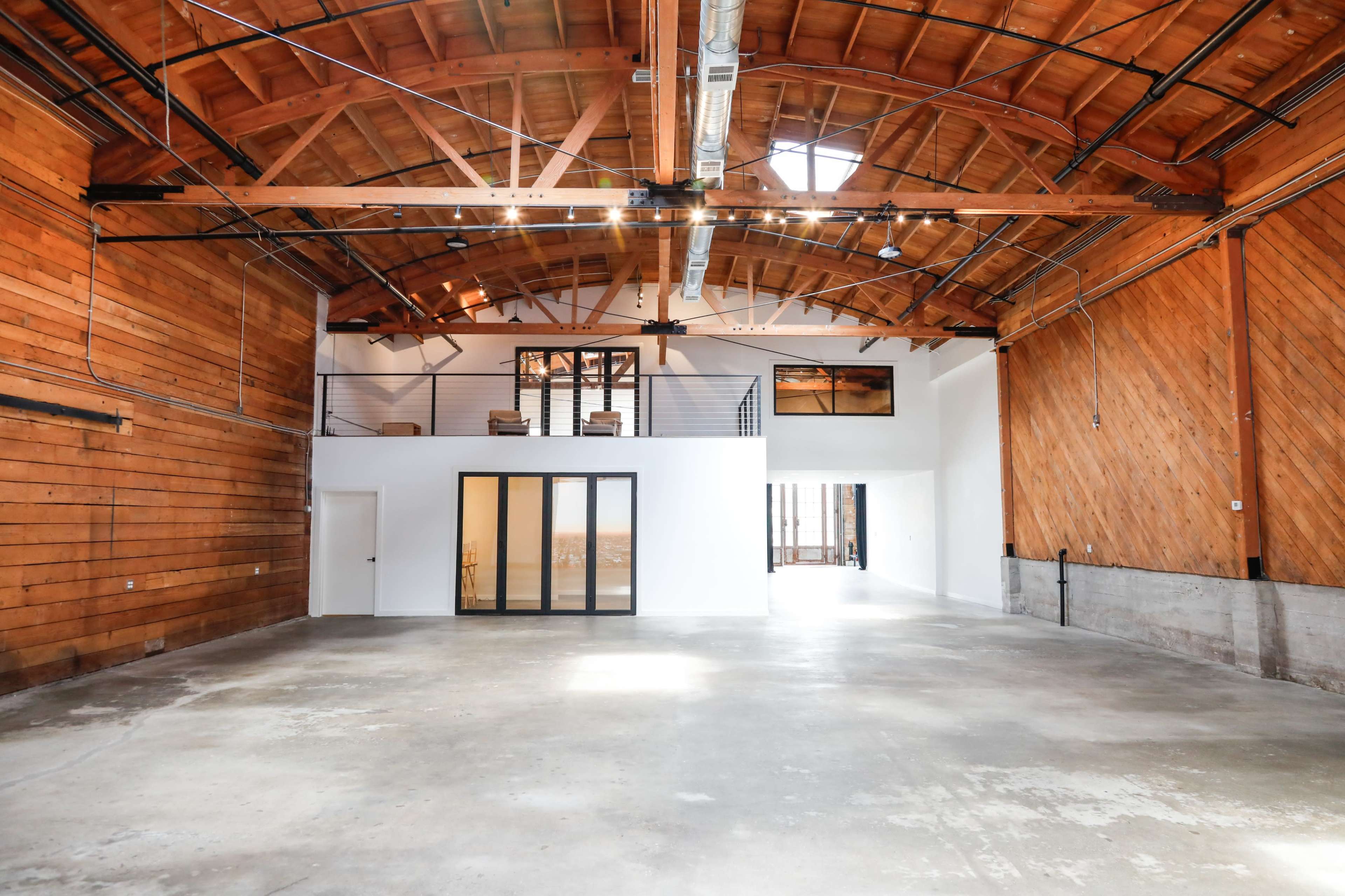 A spacious interior of a modern industrial building with wooden beams and a polished concrete floor.