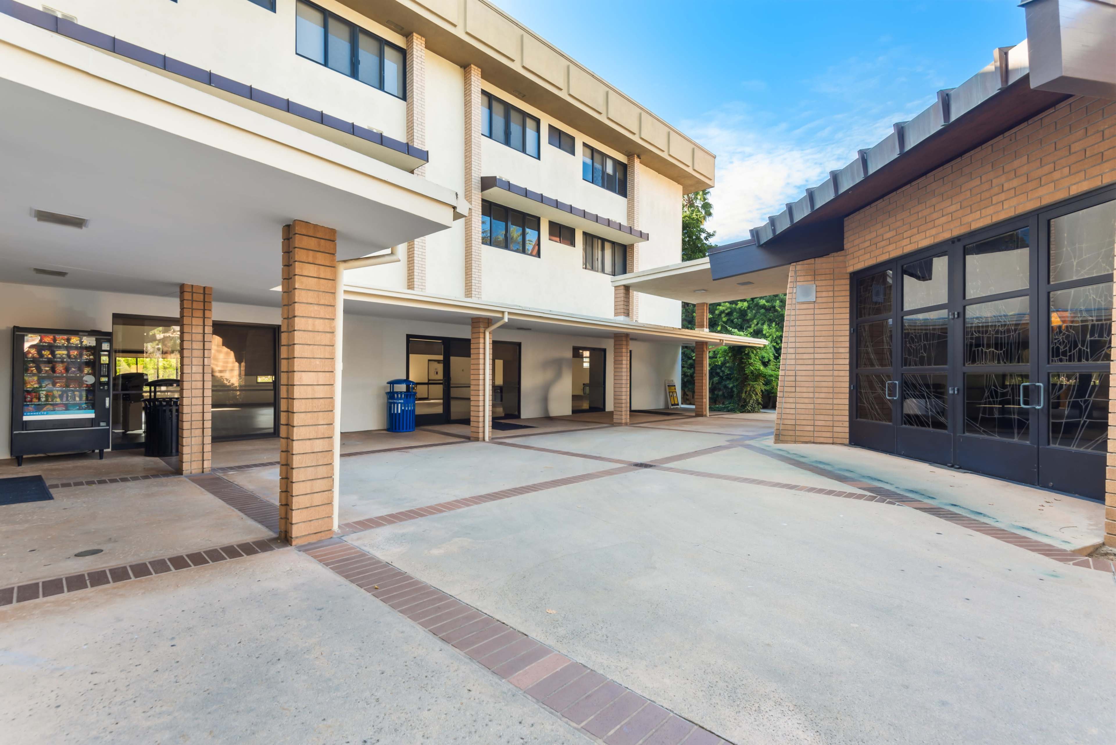 The image shows a large, open courtyard area between two buildings with a vending machine and seating areas.