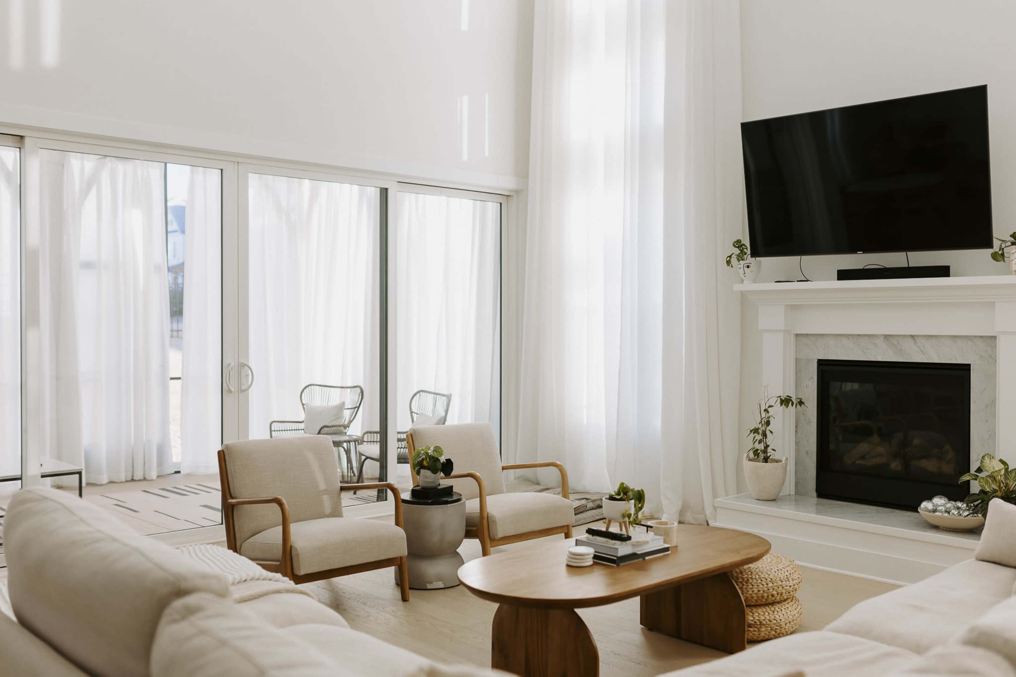The living room features a large window with sheer curtains, a cozy seating area with two armchairs, and a fireplace under a wall-mounted television.