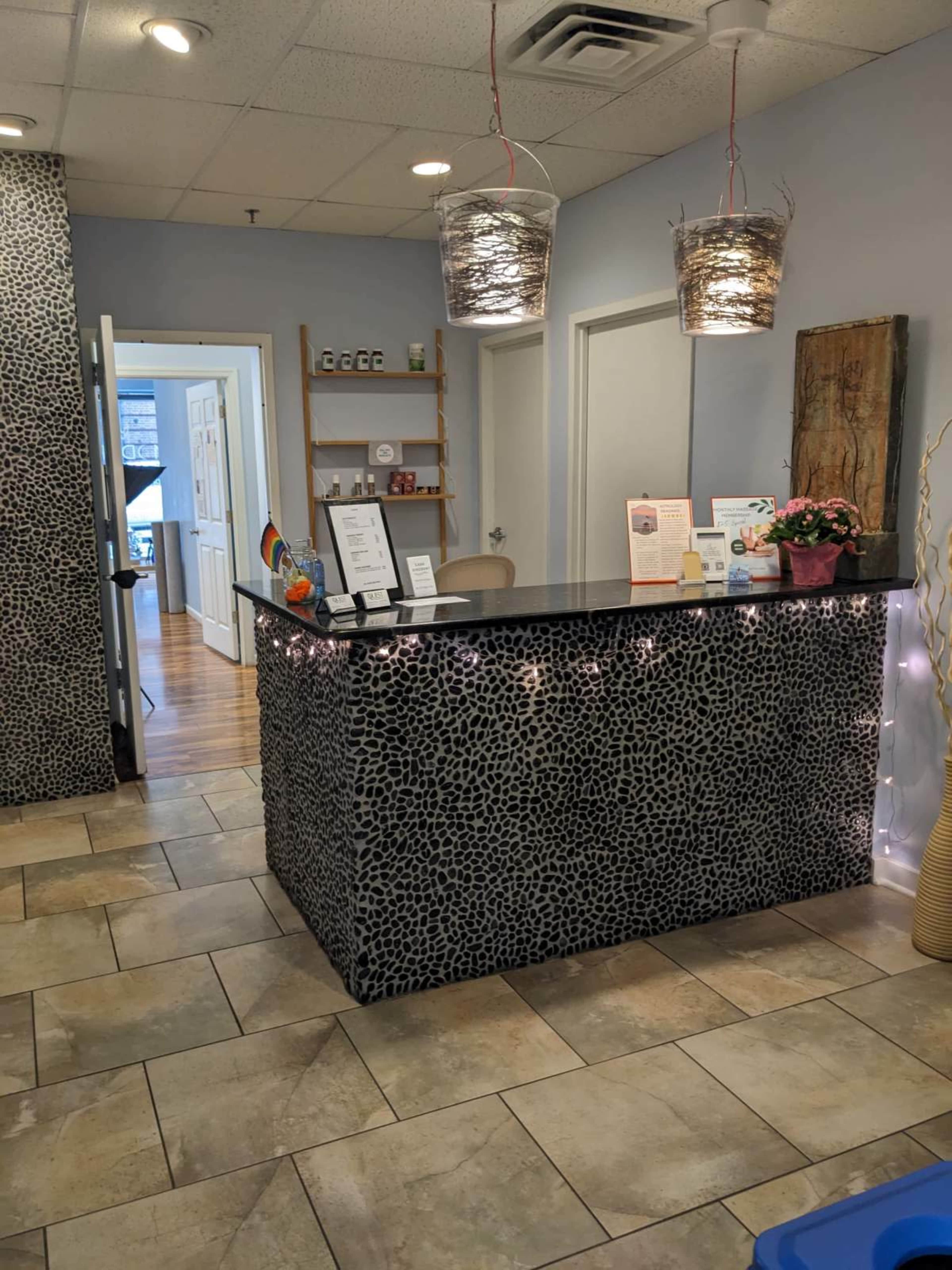 A reception area with a speckled stone counter, hanging light fixtures, and a seating area behind it.