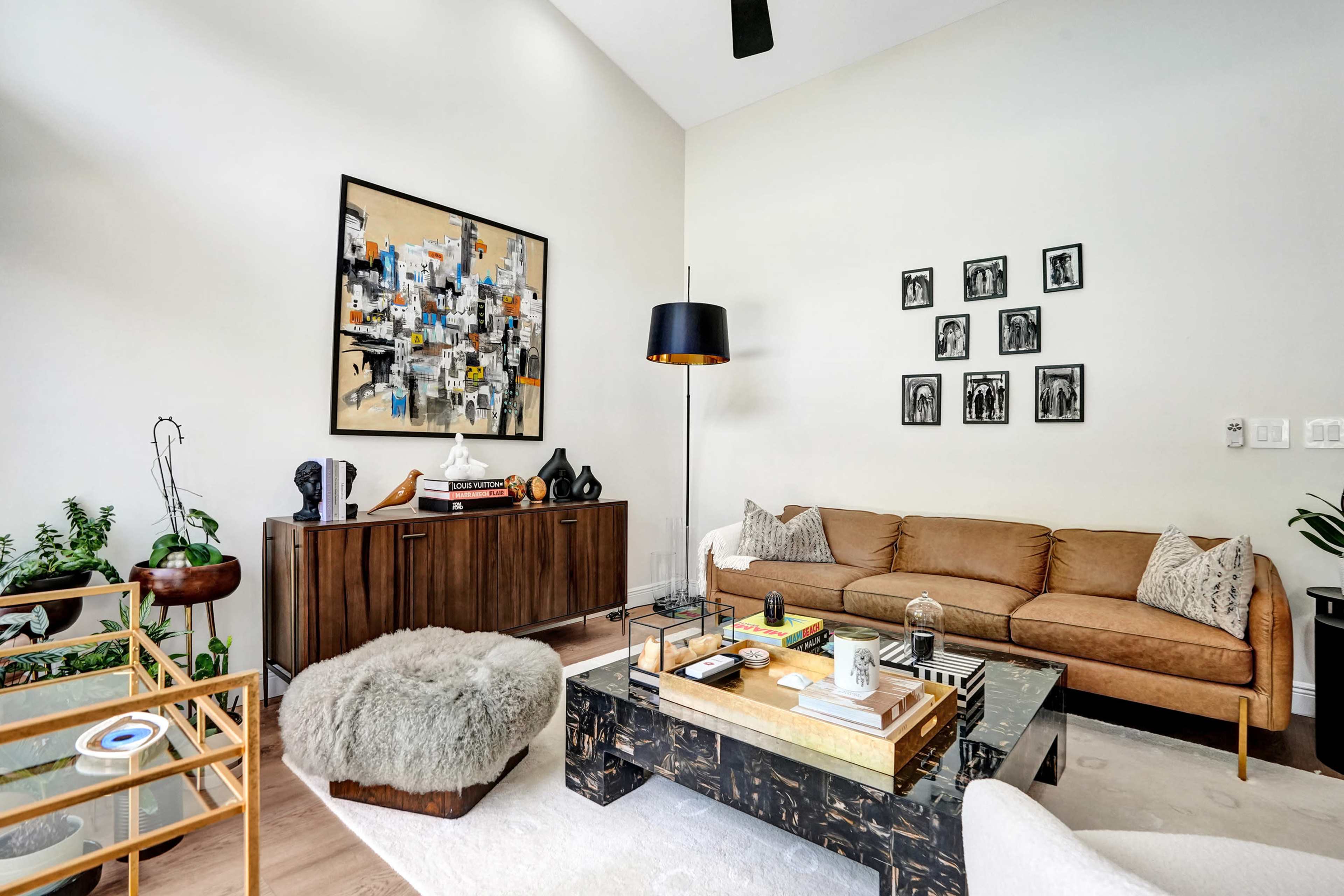 A modern living room features a beige sofa, a glass coffee table with decorative items, and an artwork hanging on the wall above a wooden sideboard.