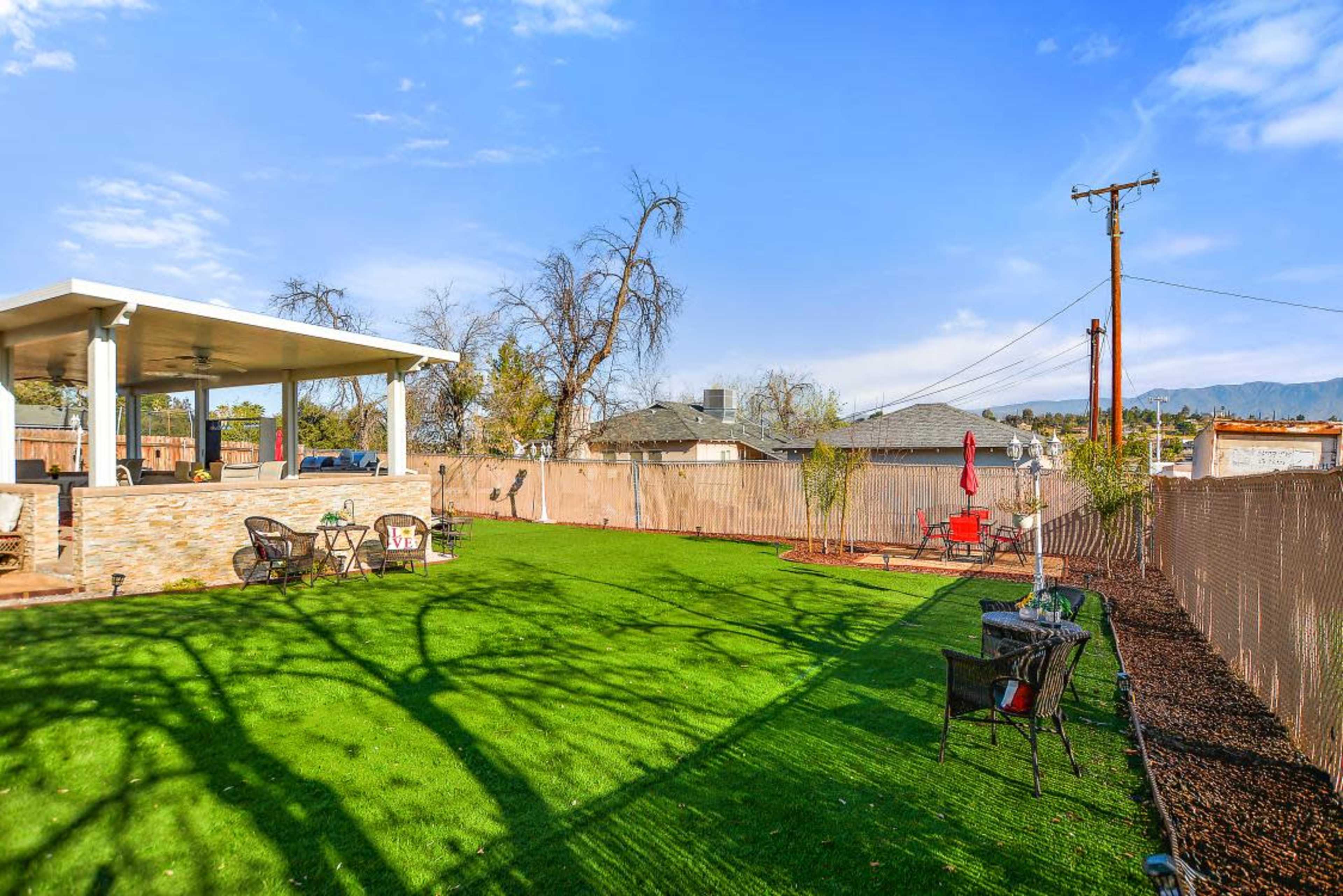 A spacious backyard featuring artificial turf, a covered patio area, and a surrounding fence.