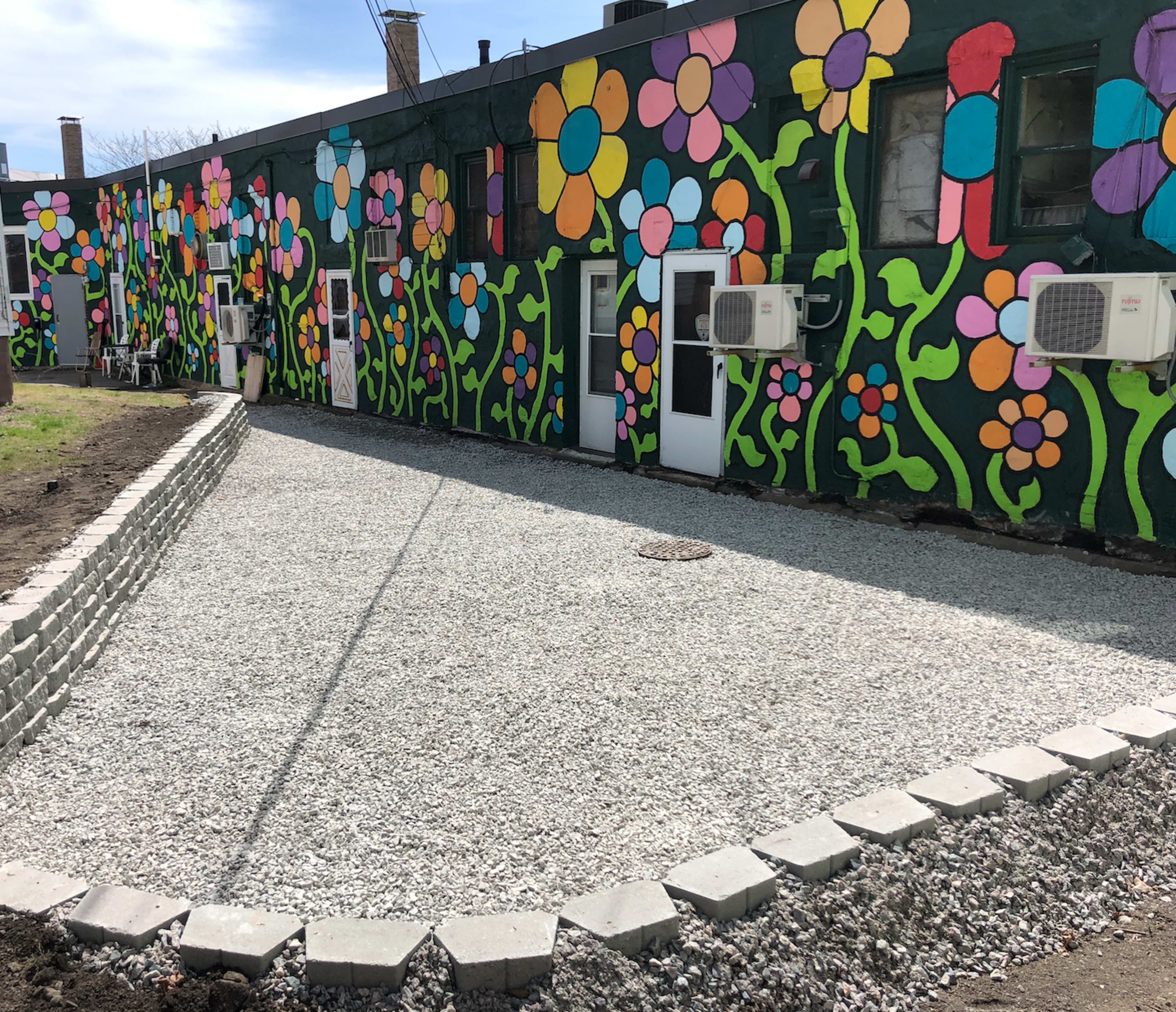A gravel courtyard with a decorative flower mural on the adjacent building's wall.