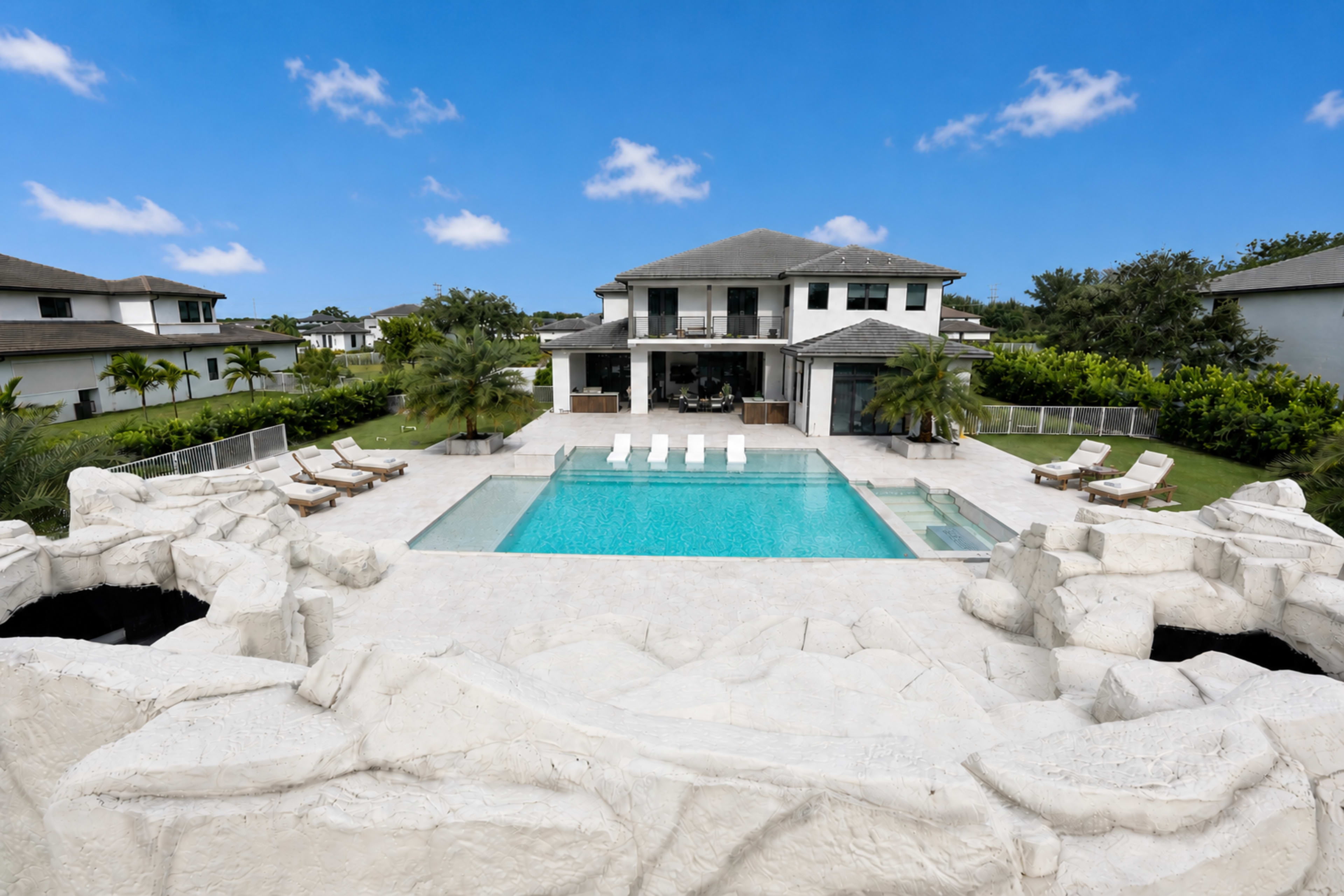 A modern two-story house with a spacious pool surrounded by lounge chairs and landscaped gardens.