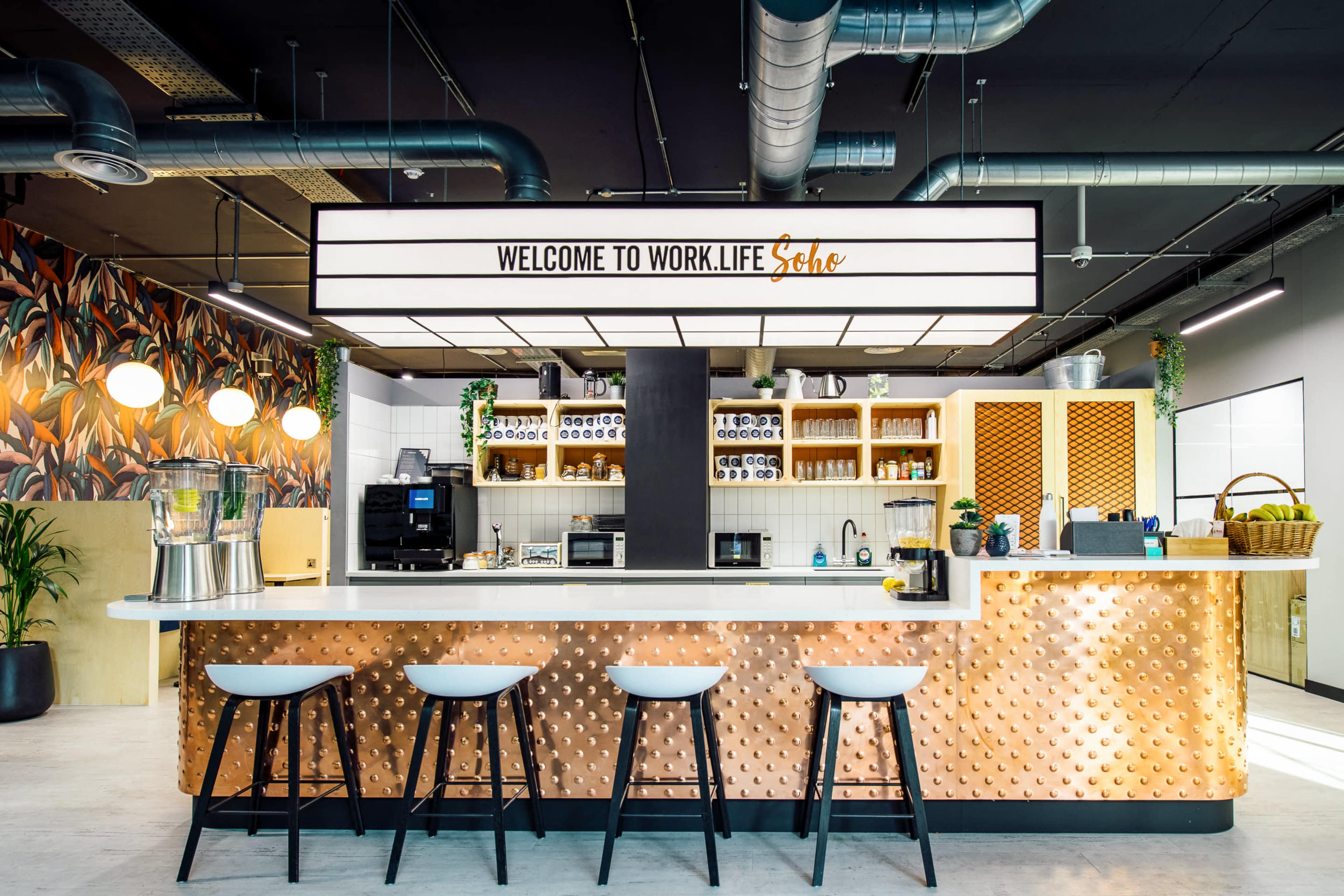 A modern kitchen area with a welcoming sign, a bar with stools, and shelves filled with various kitchen appliances and decor.