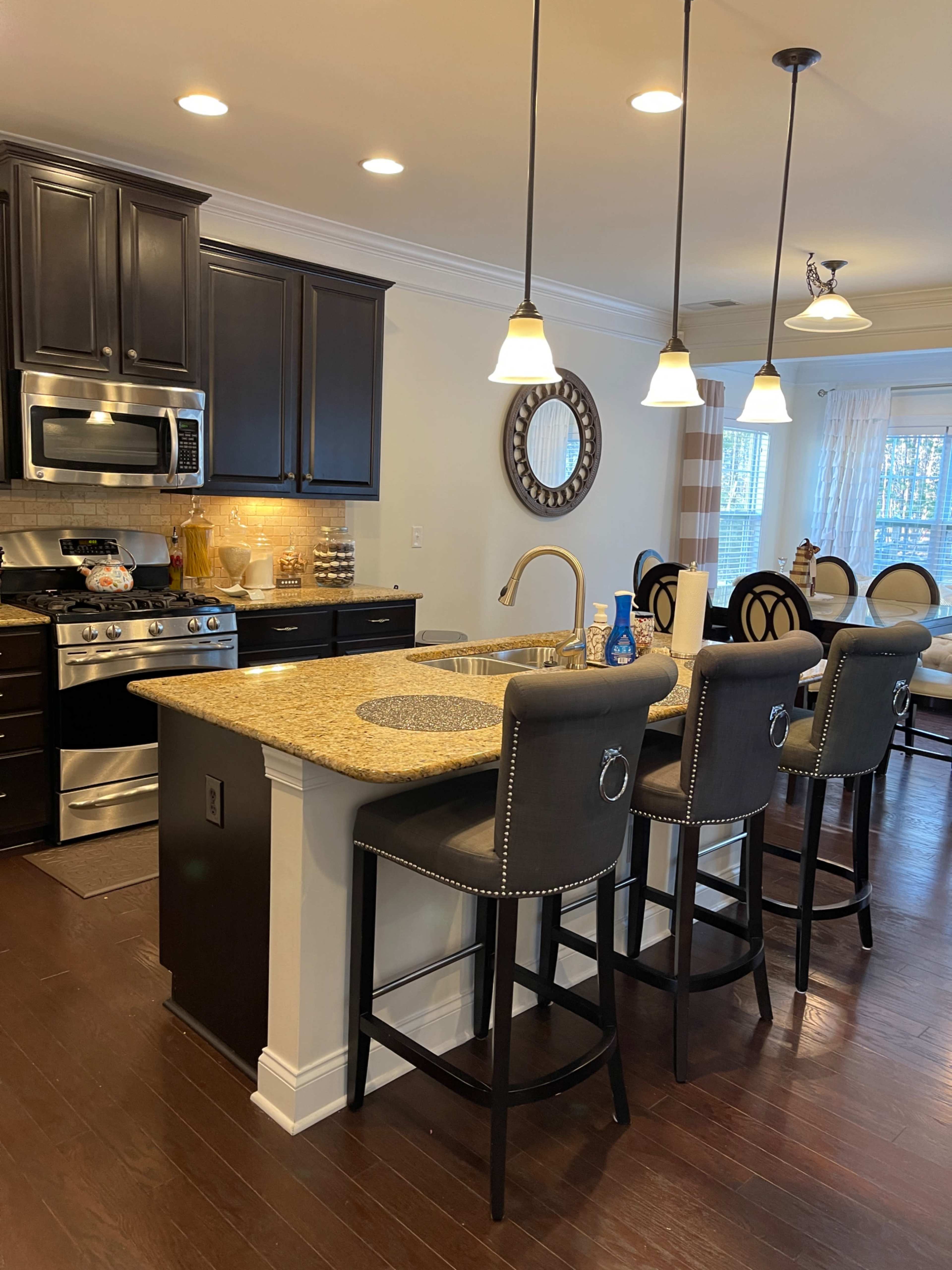 A modern kitchen with dark cabinetry, a granite island with seating, and pendant lights above.