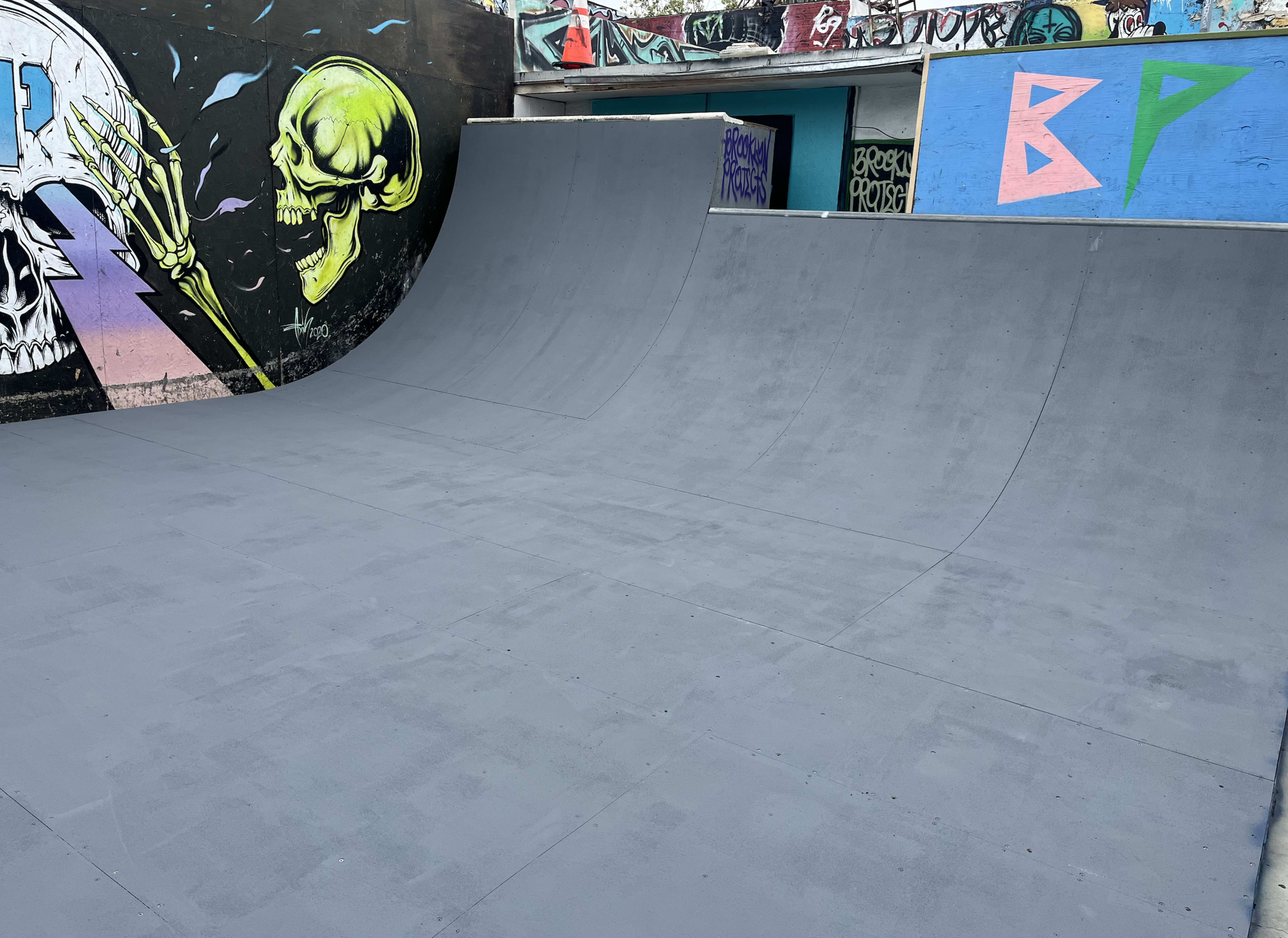 The image shows a gray skate ramp in front of a graffiti-covered wall featuring colorful skull artwork.