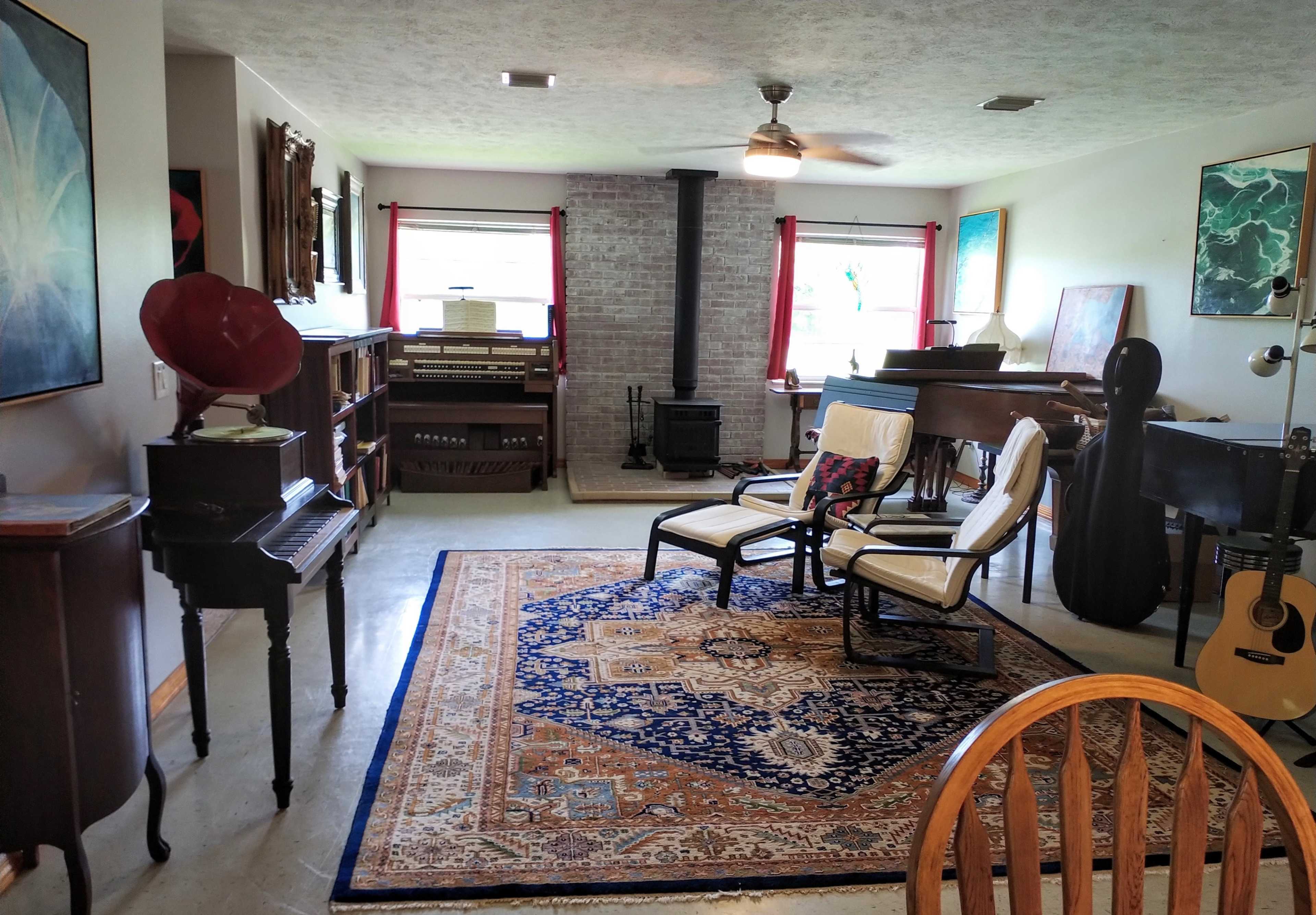 The room features a cozy living space with a wood stove, comfortable seating, musical instruments, and various artworks adorning the walls.