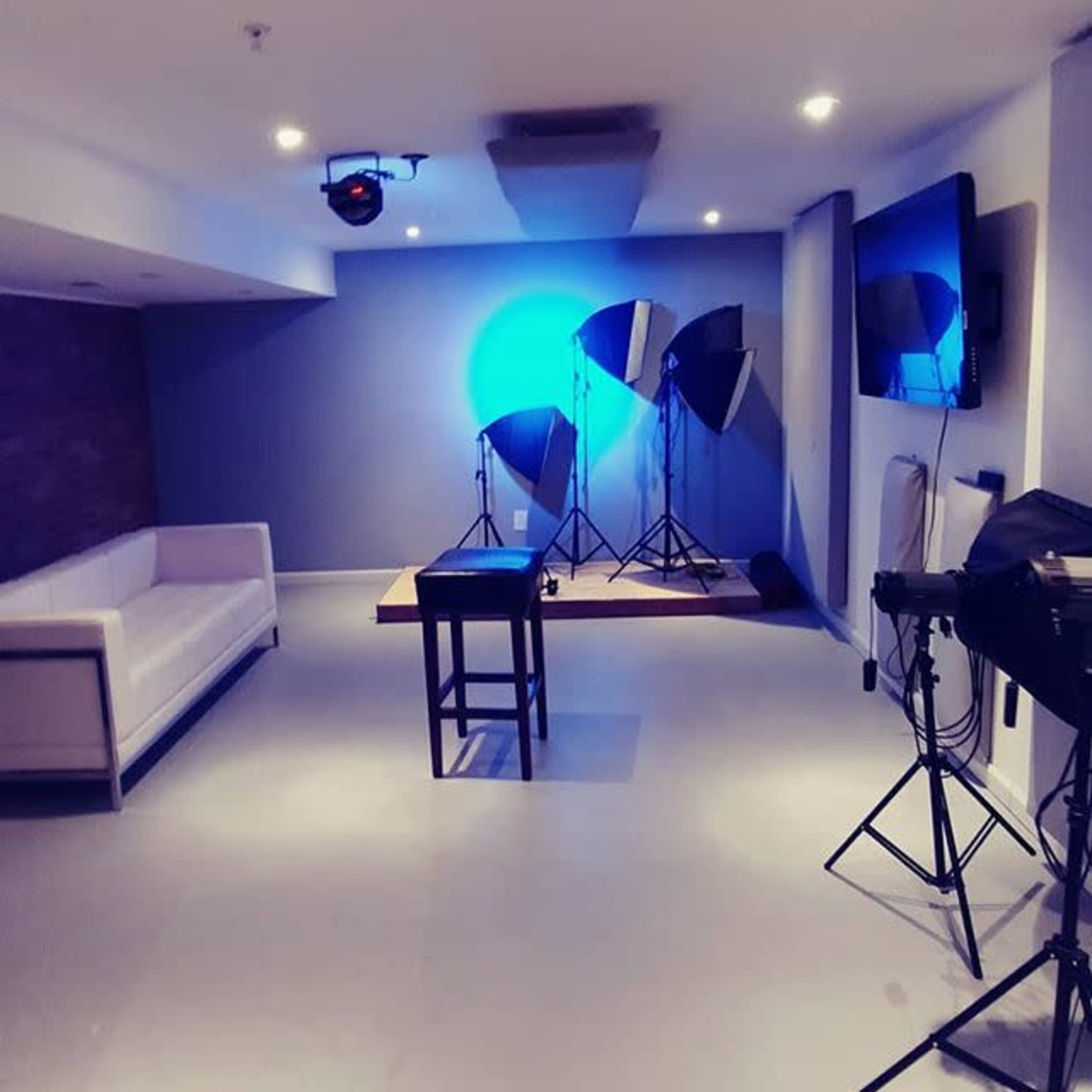 The room features a white couch, a small table, and multiple photography lights on tripods, all set against a neutral backdrop.