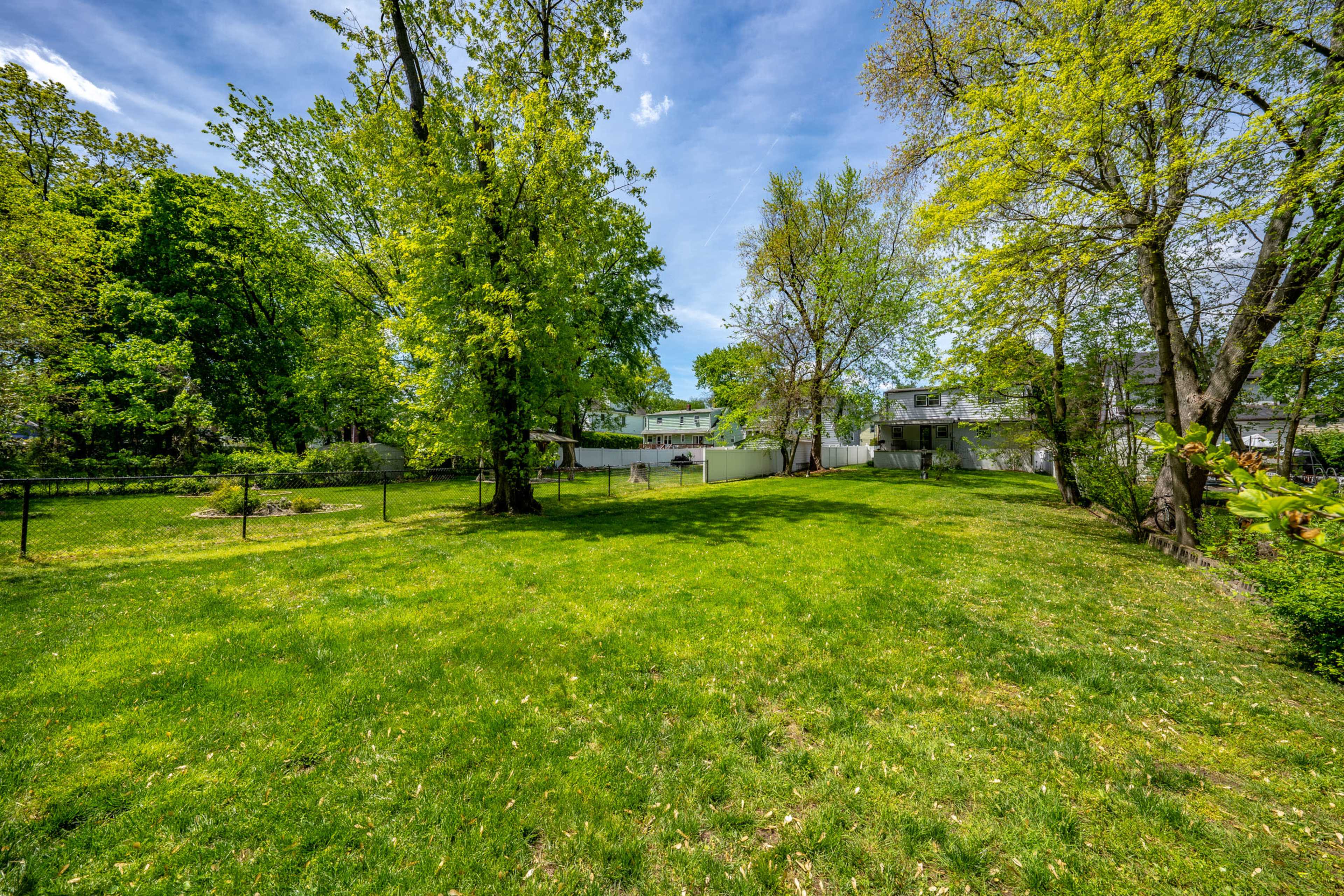 A spacious green yard is surrounded by trees, with a few houses visible in the background.