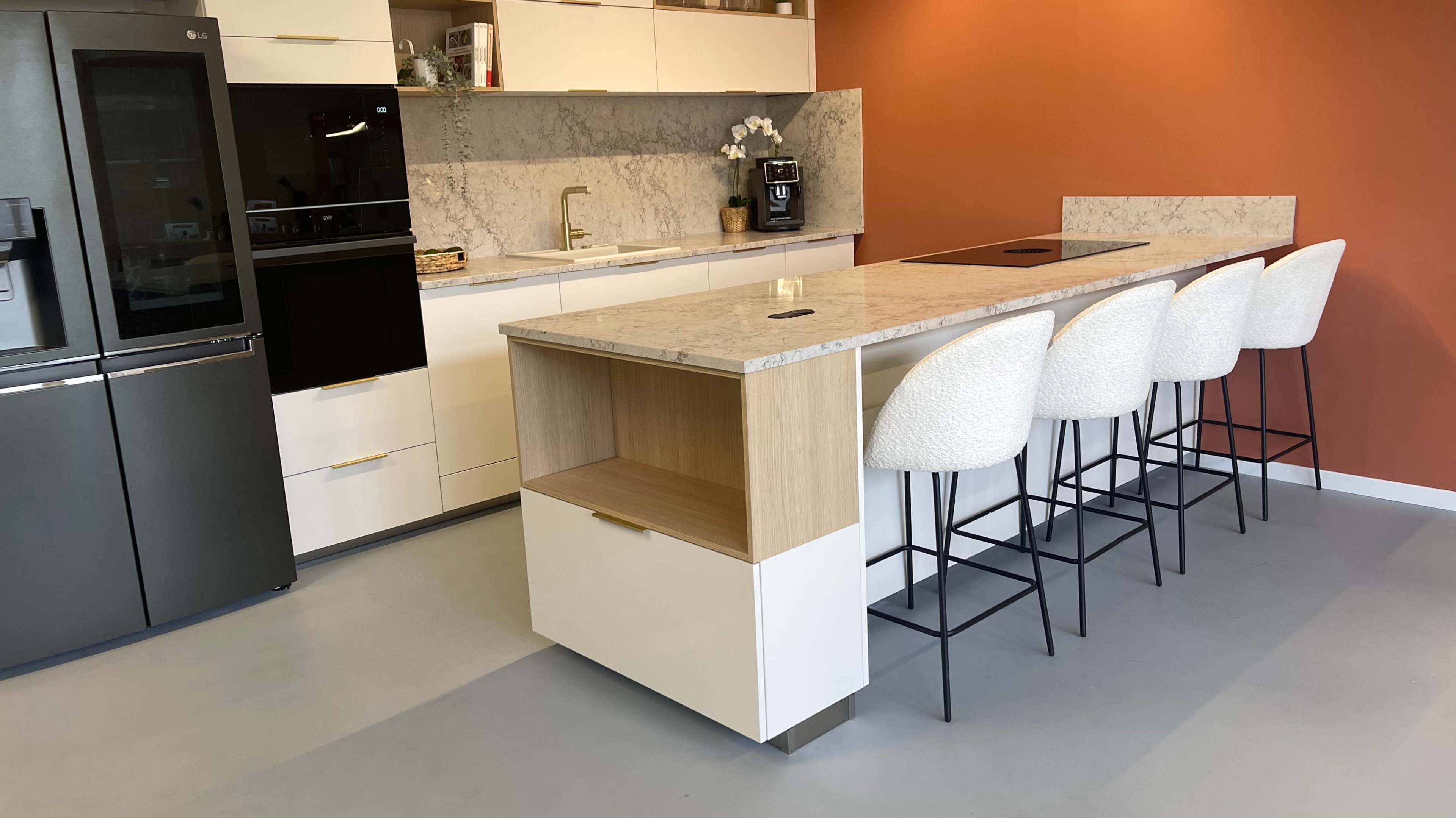 The image shows a modern kitchen with a large island featuring a marble countertop and five white bar stools, against a backdrop of orange and light-colored cabinets.