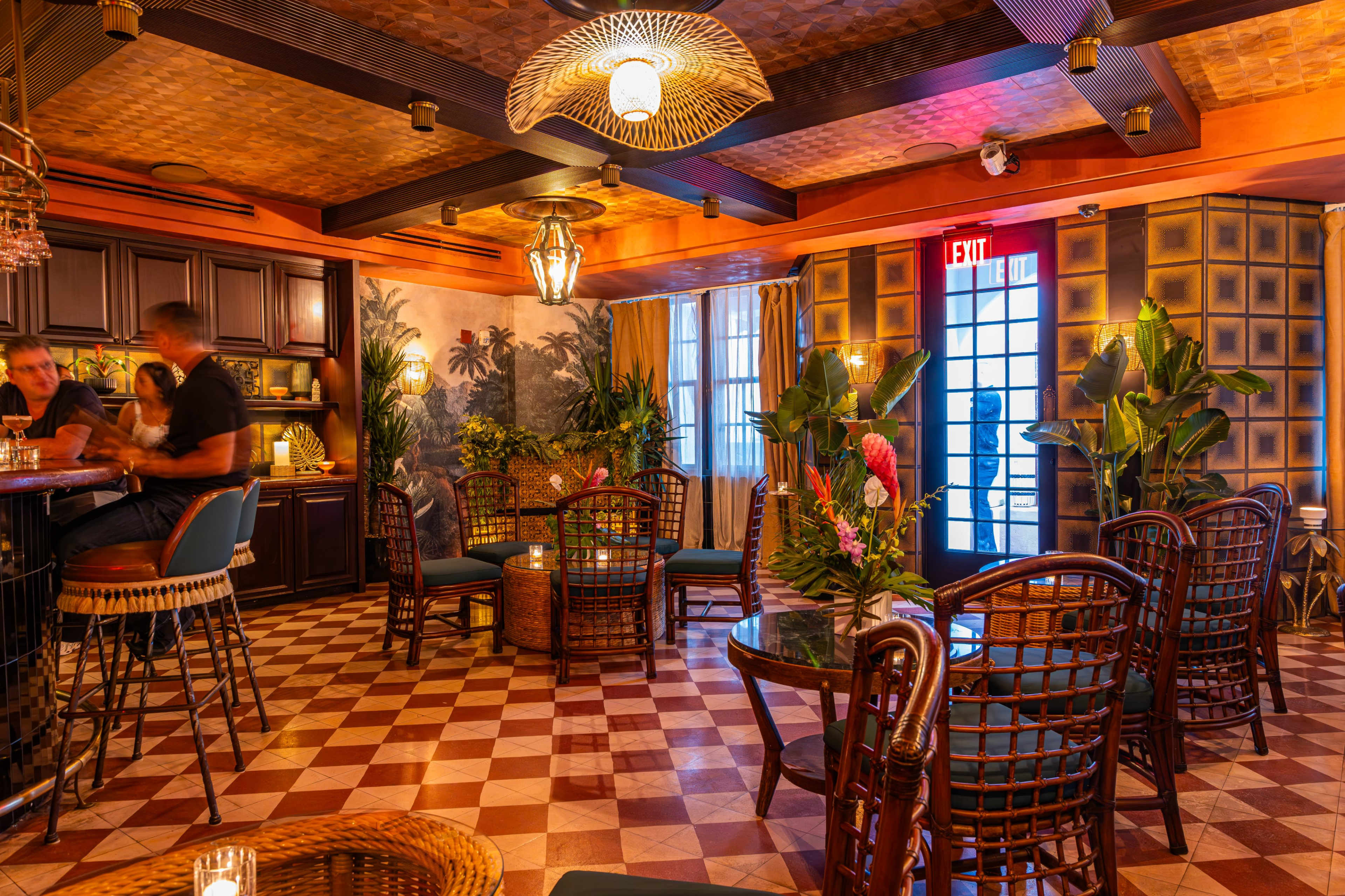 The image depicts a vibrant bar and lounge area with patterned tile flooring, tropical decor, and a mix of seating options.