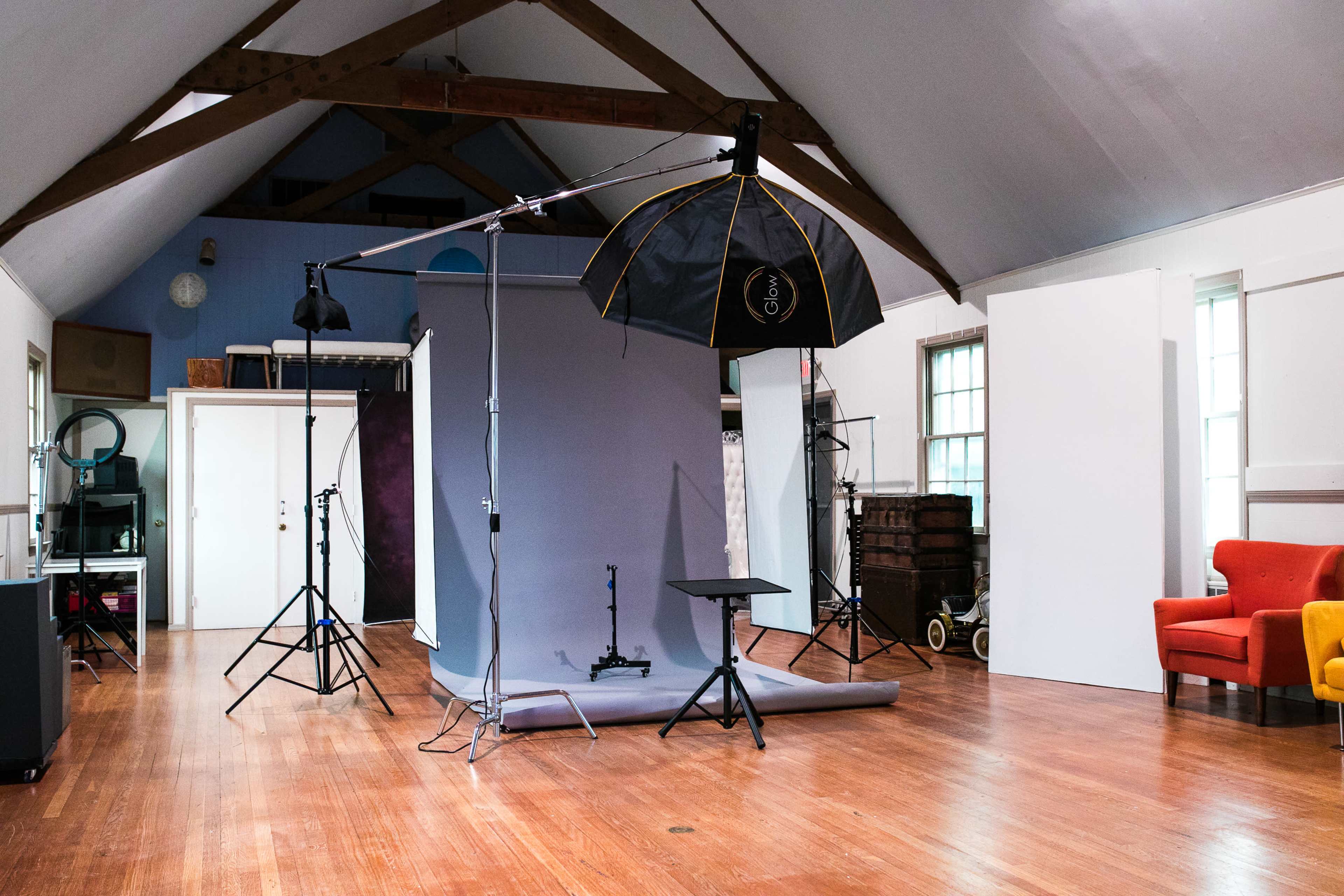 A photography studio with a backdrop, lighting equipment, and empty spaces around a wooden floor.