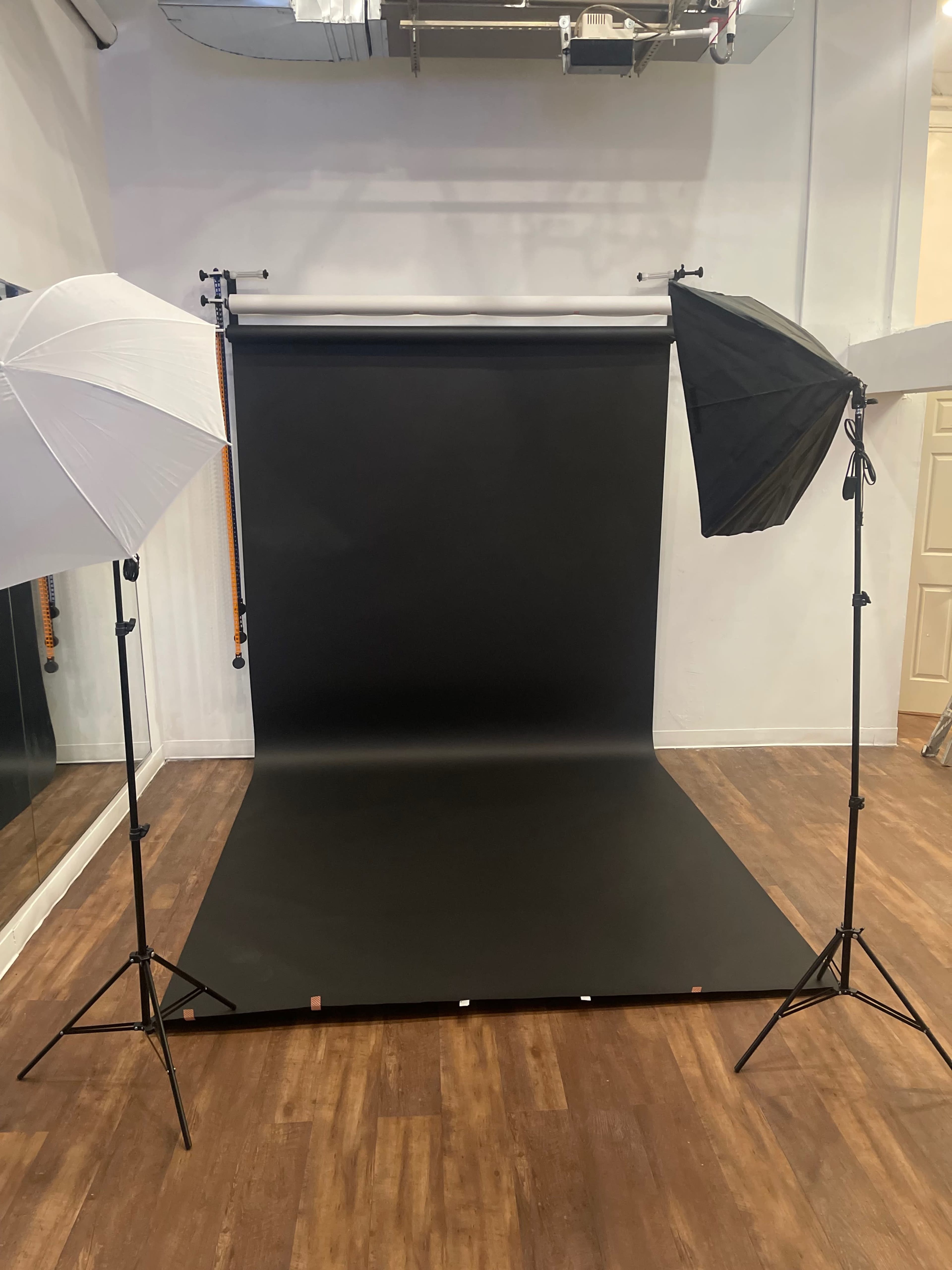 A photography studio set up with a black background, two light stands equipped with softboxes, and a wooden floor.