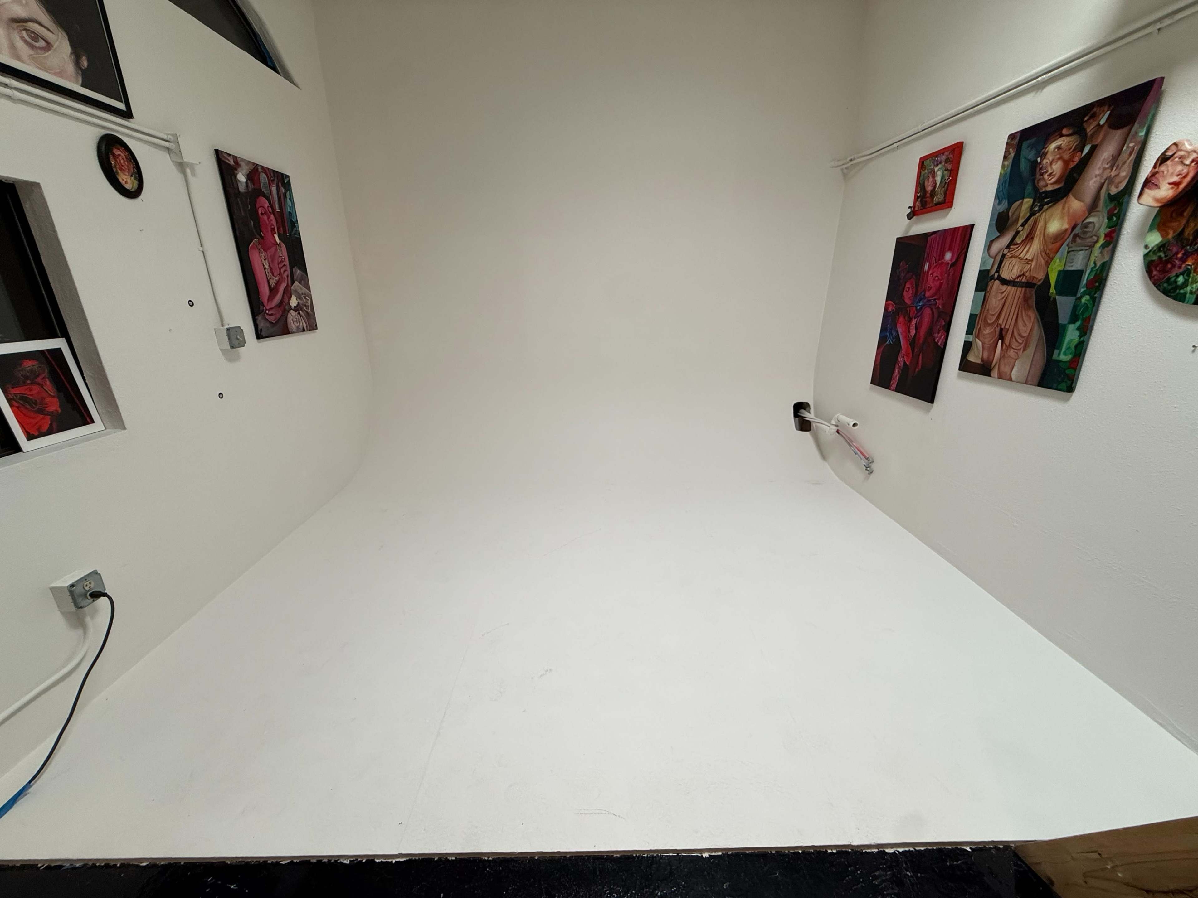 The image shows a white-walled gallery space featuring several colorful paintings framed on two walls.