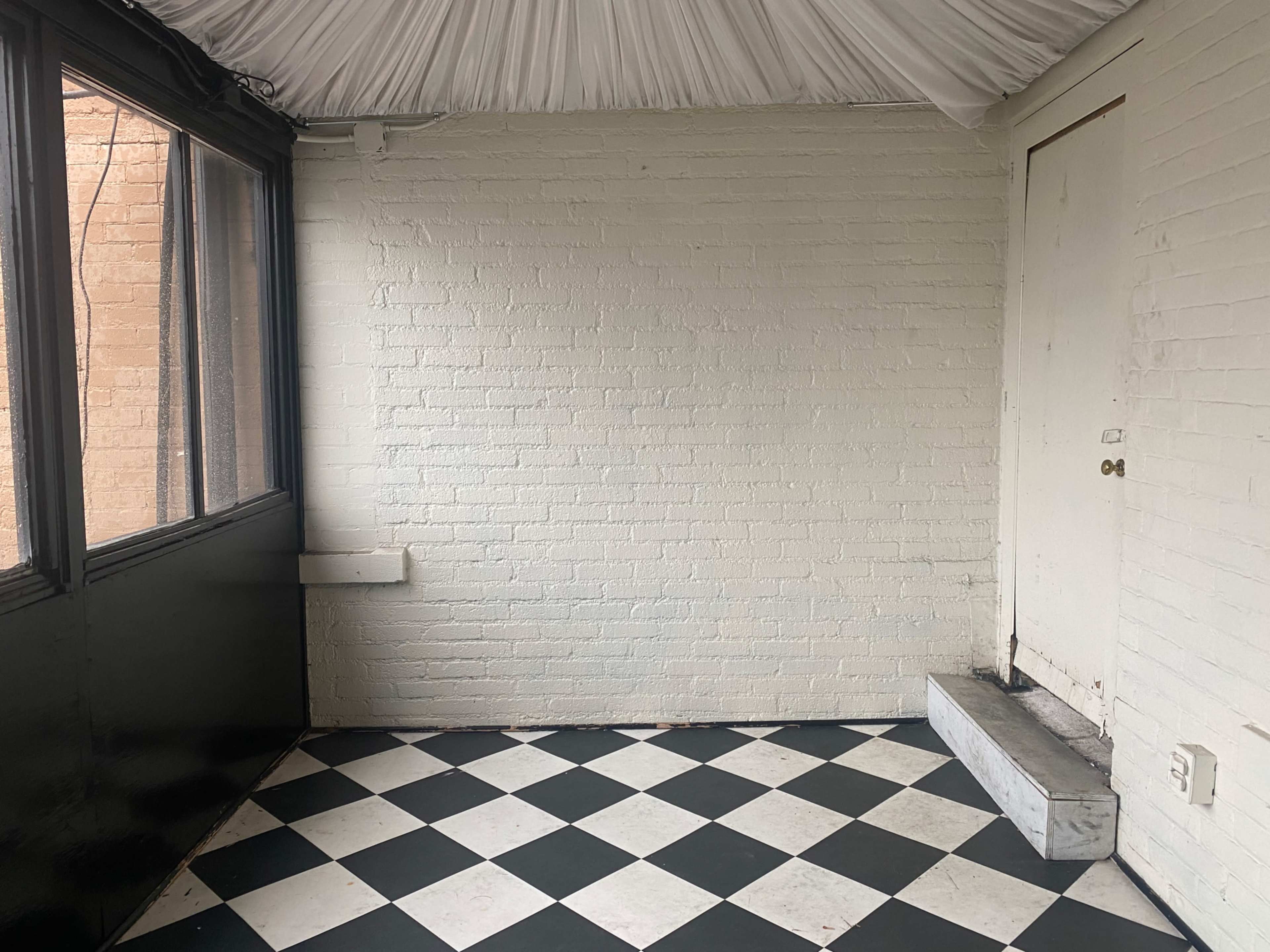 An empty room with a checkered black and white floor, white brick walls, and a door at the far end.
