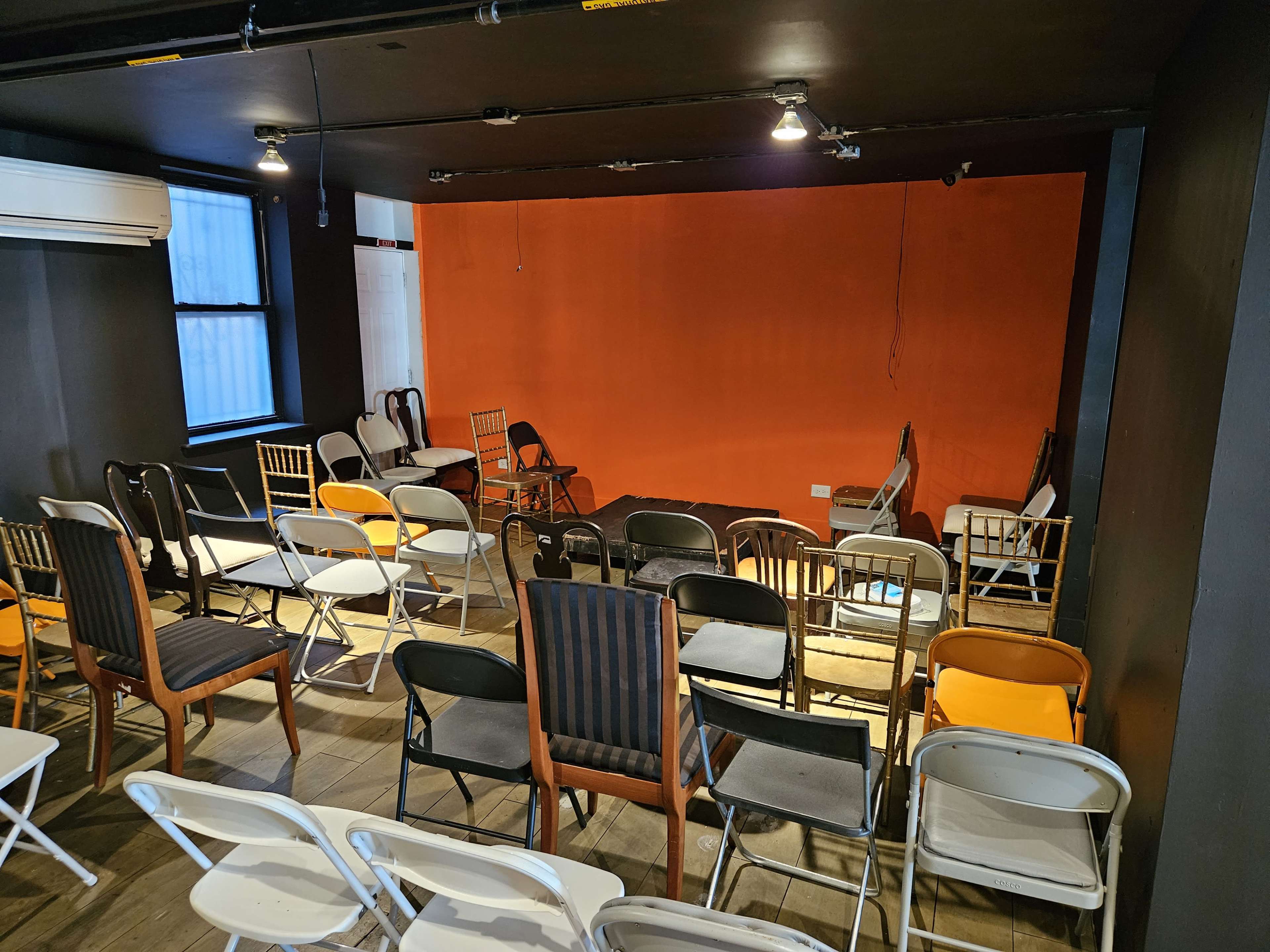 A room with an orange accent wall is arranged with various types of chairs set up for an event.