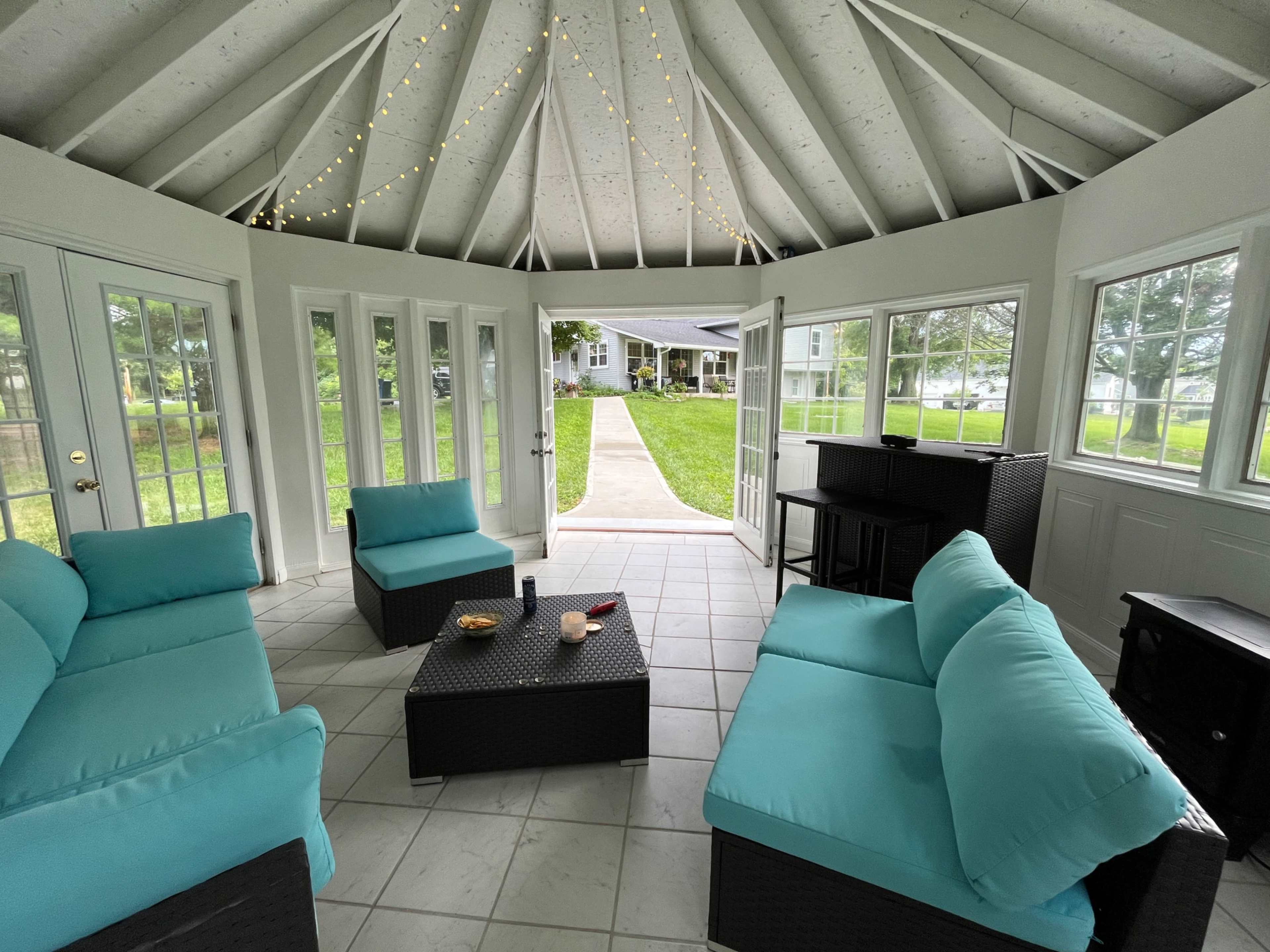 A sunlit gazebo with turquoise seating and a pathway leading to a grassy area visible through open doors.