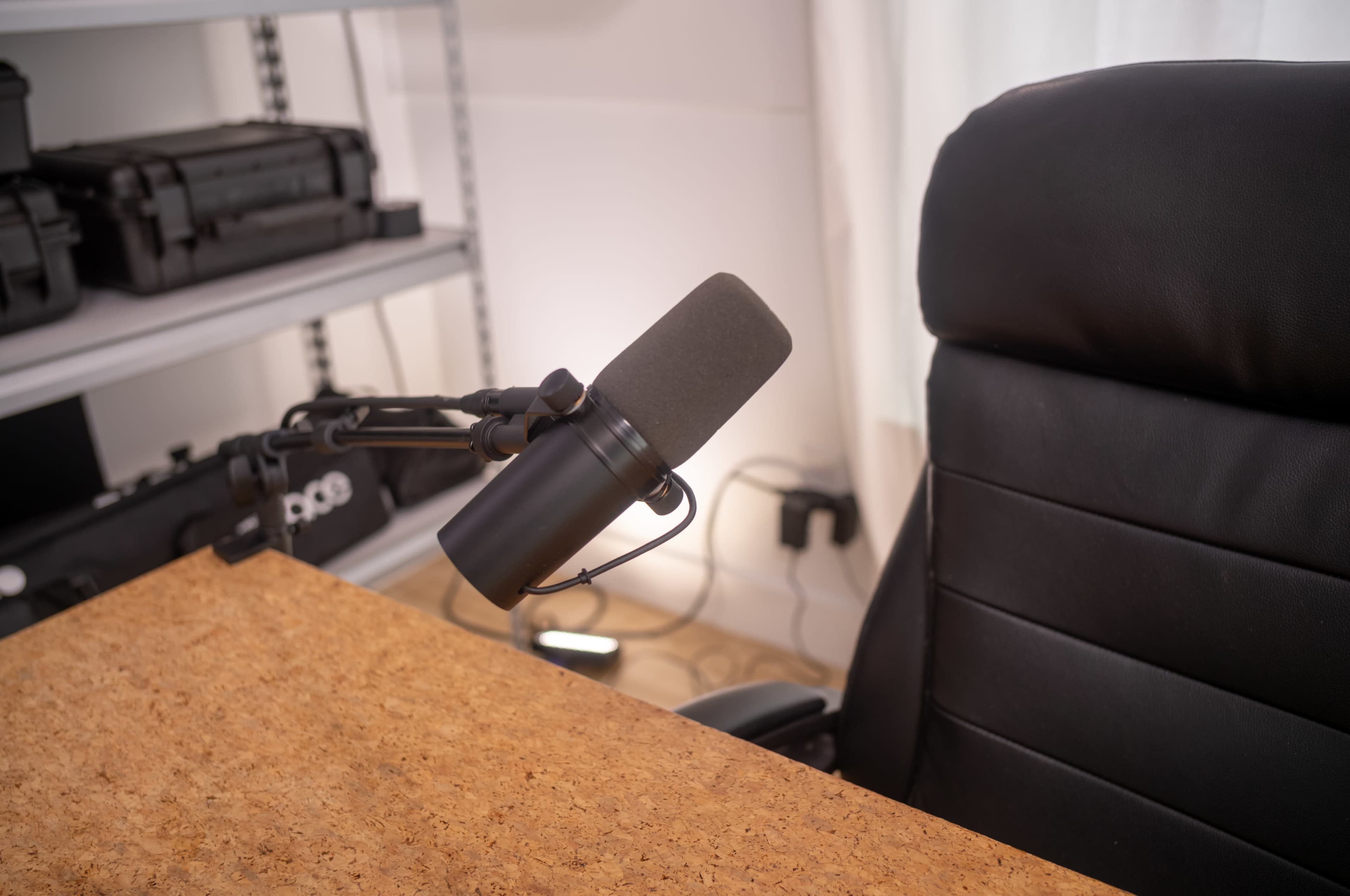 A black microphone is mounted on an adjustable arm next to an empty black office chair at a wooden desk.