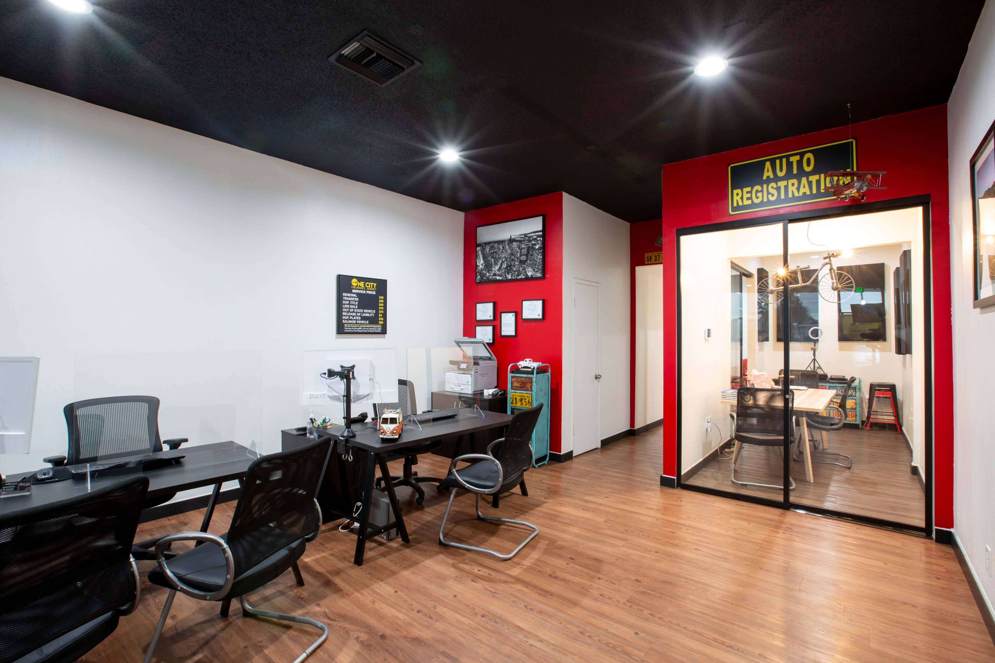 A modern office space with several workstations, a glass-enclosed meeting room, and a bright red accent wall.