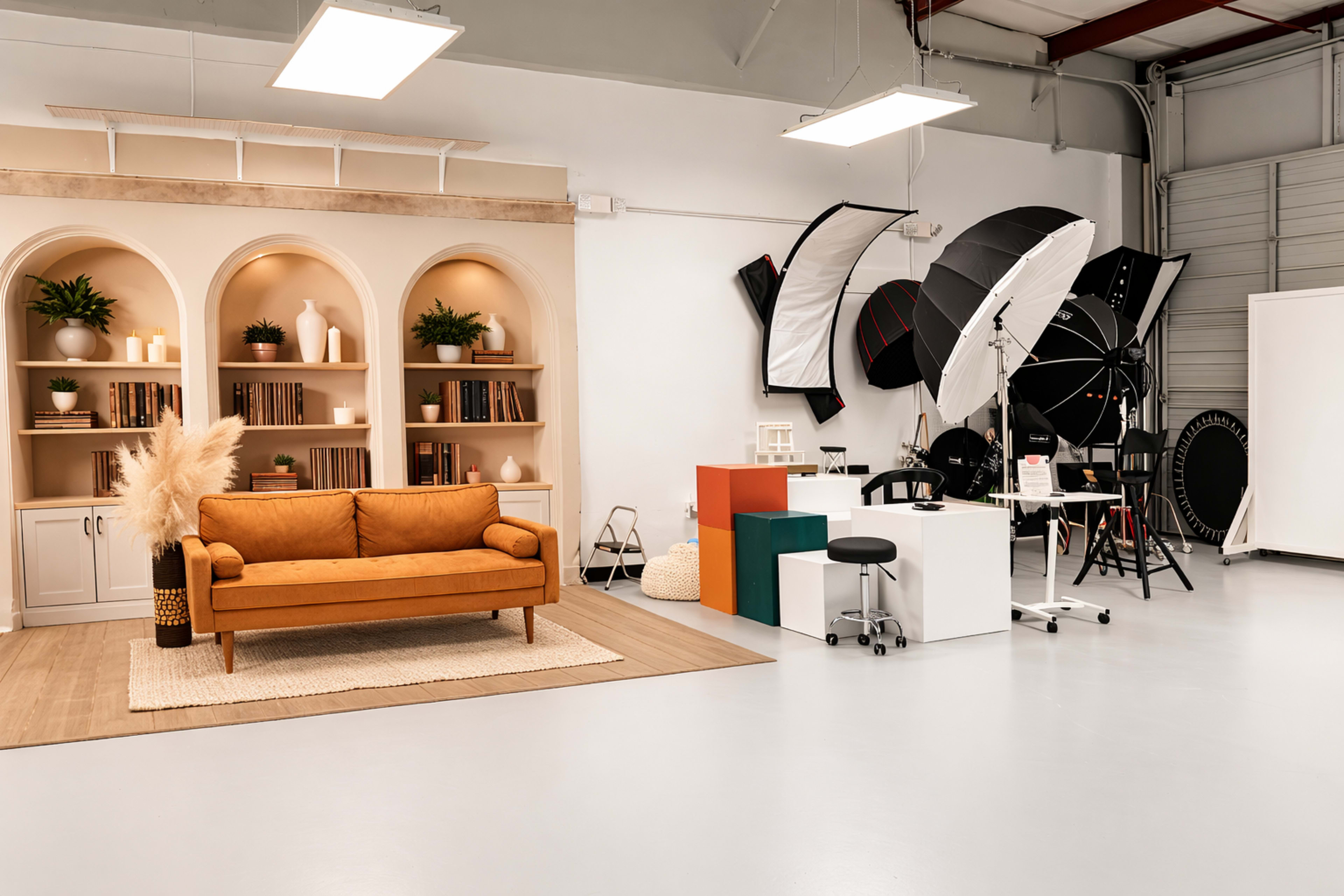 The image shows a well-organized studio space featuring a brown couch, decorative bookshelves, and photography equipment arranged on one side of a light-colored floor.