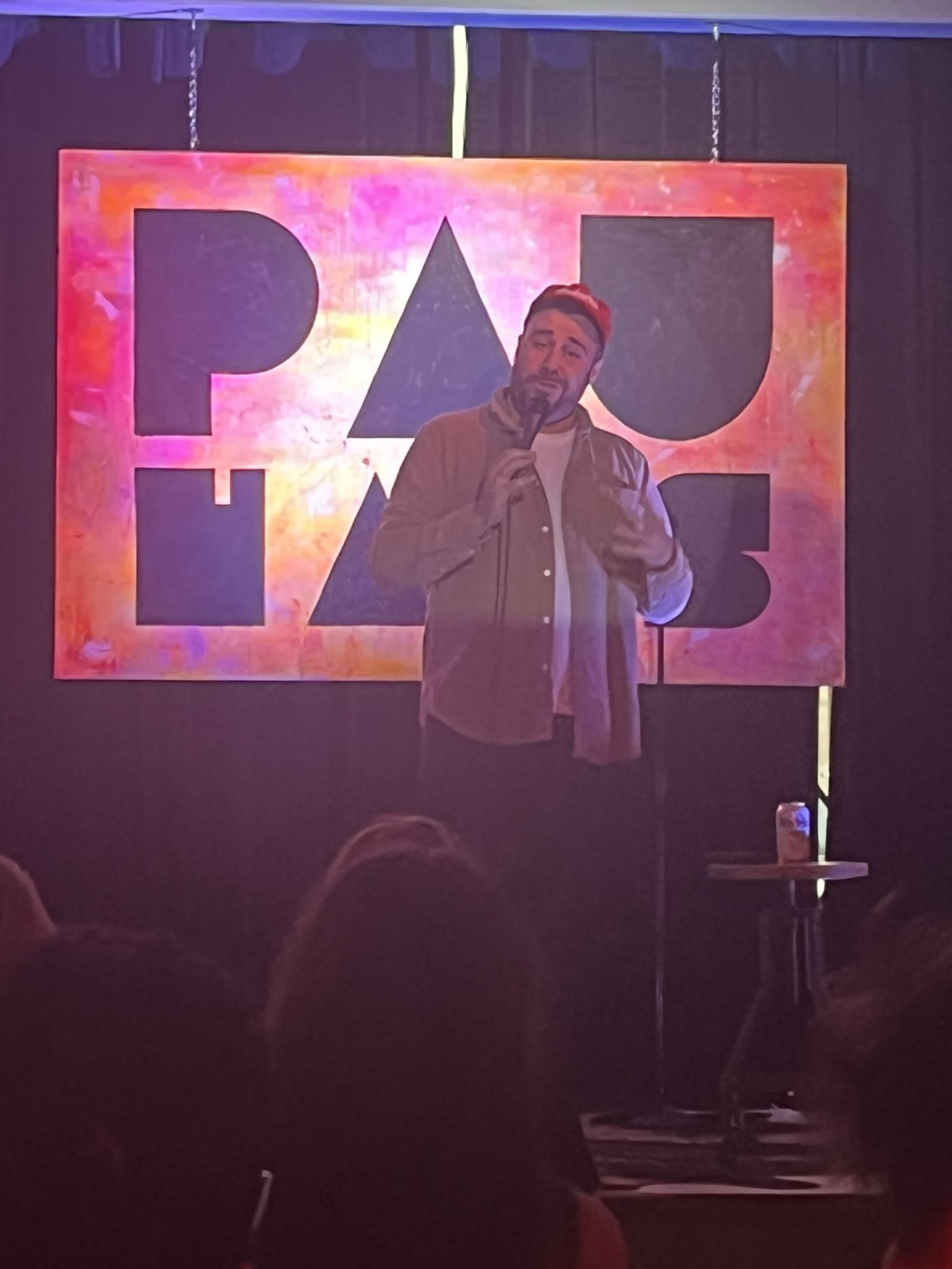 A comedian performs on stage in front of a colorful backdrop at a comedy club.
