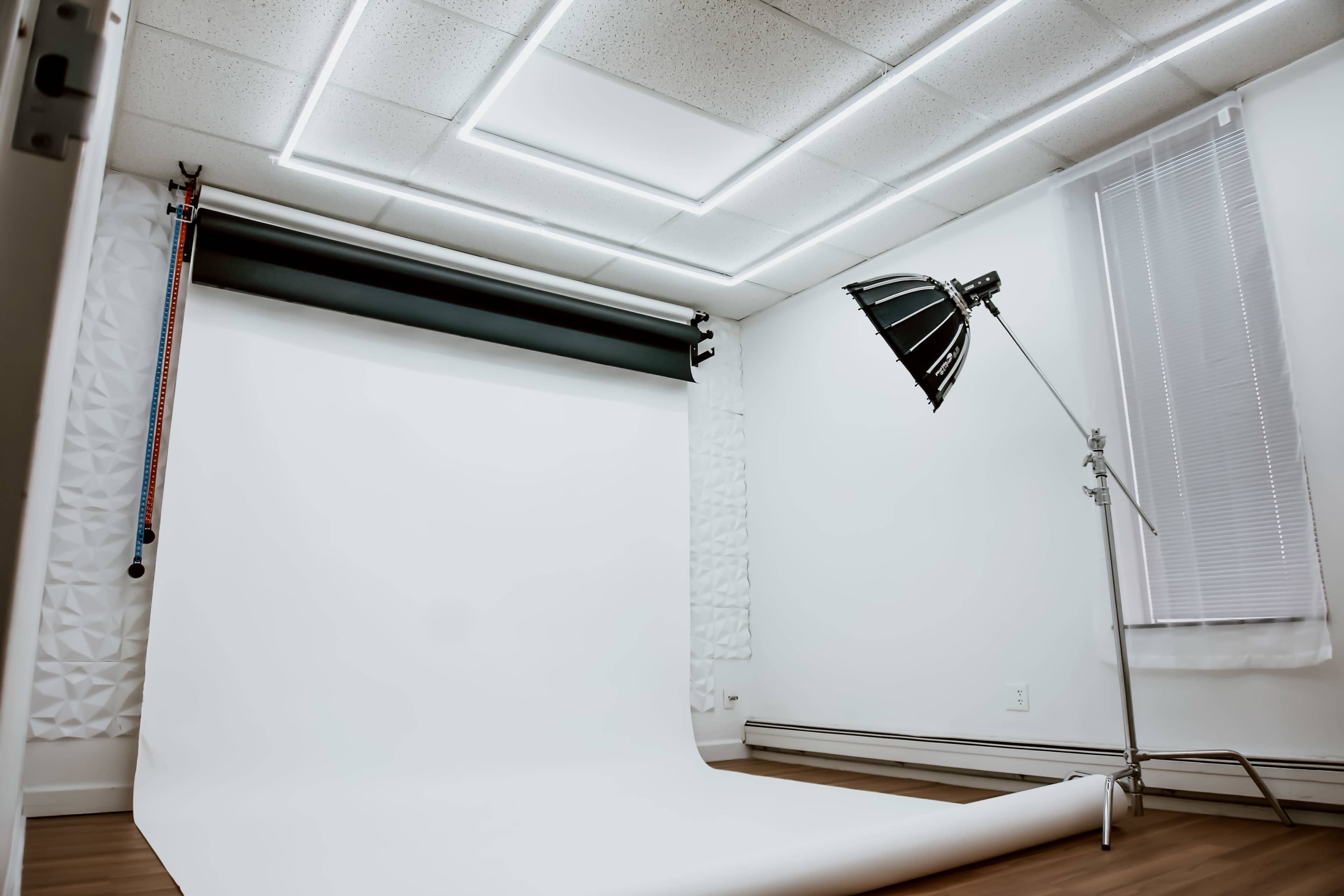 A photography studio features a white backdrop, floor, and a large lamp on a stand.