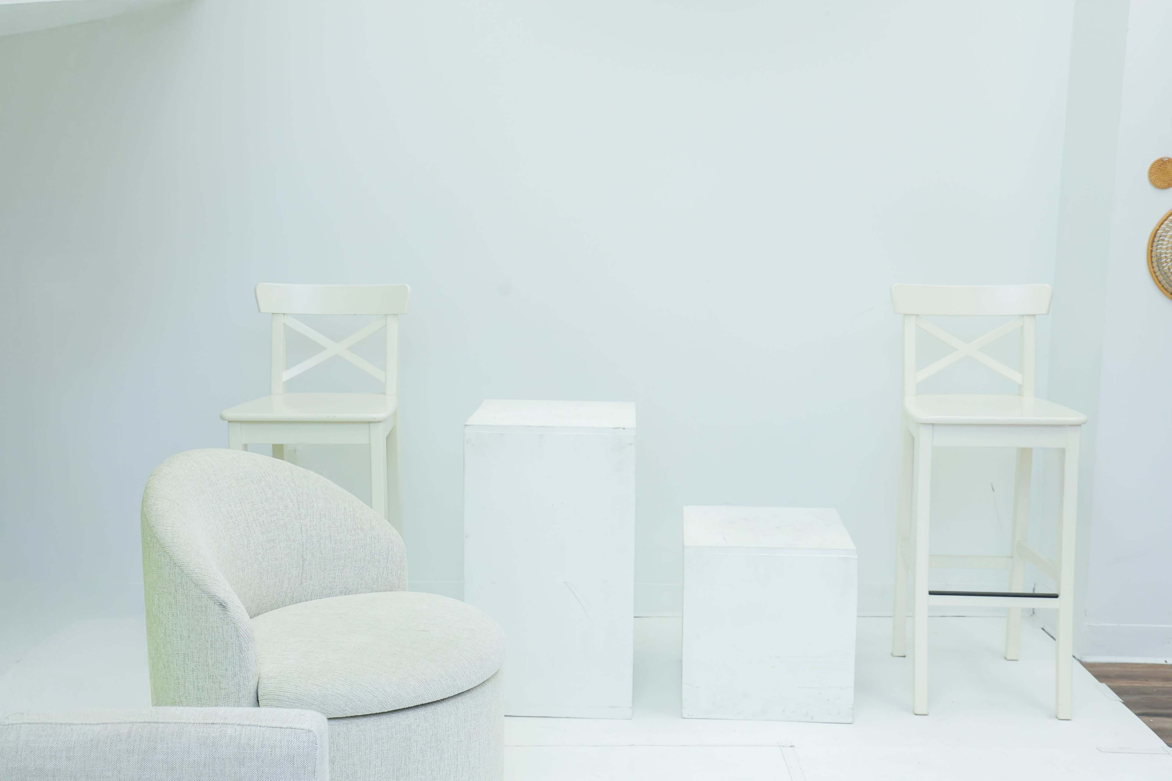 The scene features two white chairs and two white boxes placed against a plain wall, with a soft grey upholstered chair in the foreground.