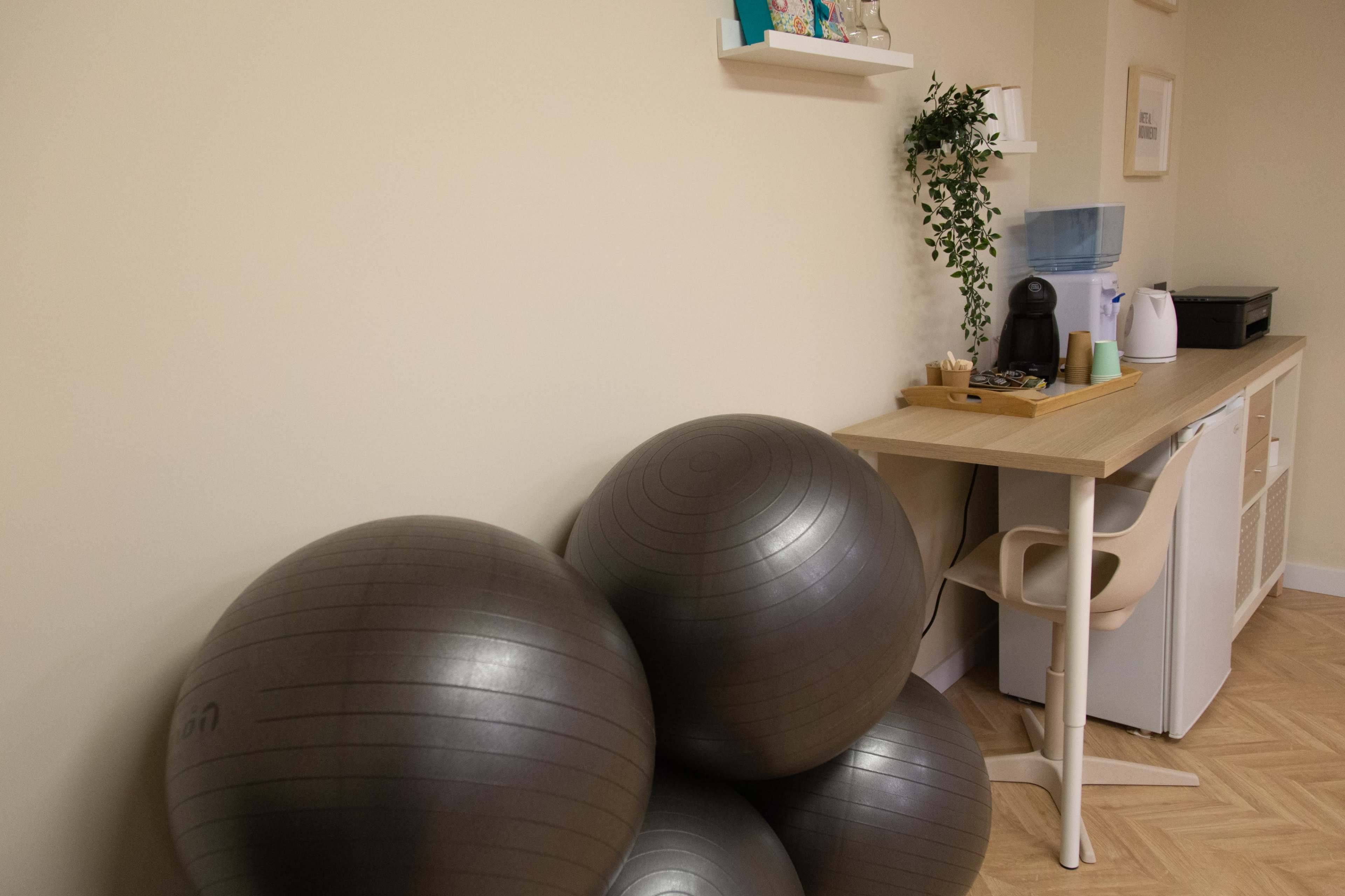 A stack of three gray exercise balls is positioned next to a small kitchen area with a countertop and appliances.