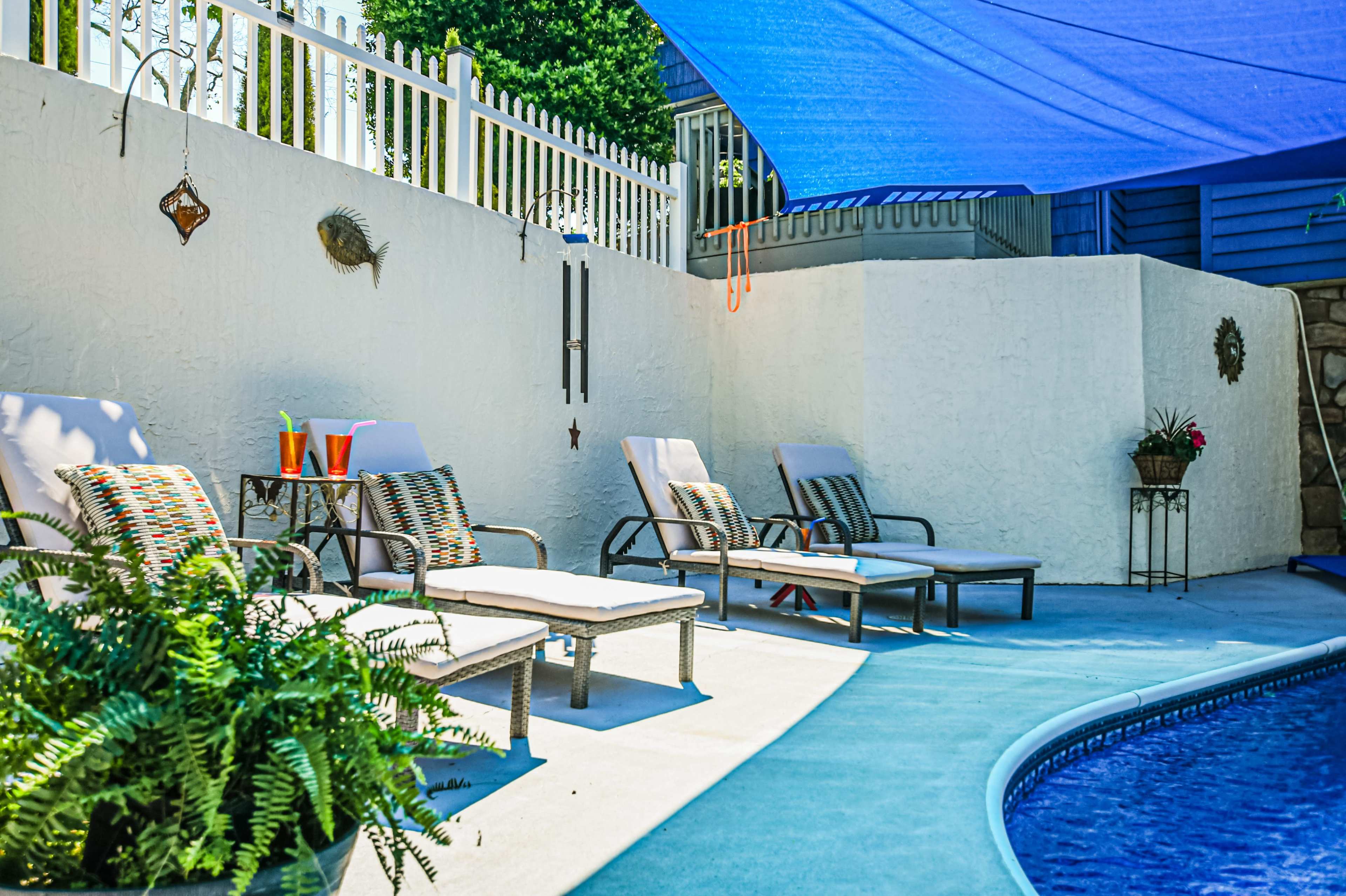 A poolside area equipped with lounge chairs, a shaded section, and decorative plants against a white wall.