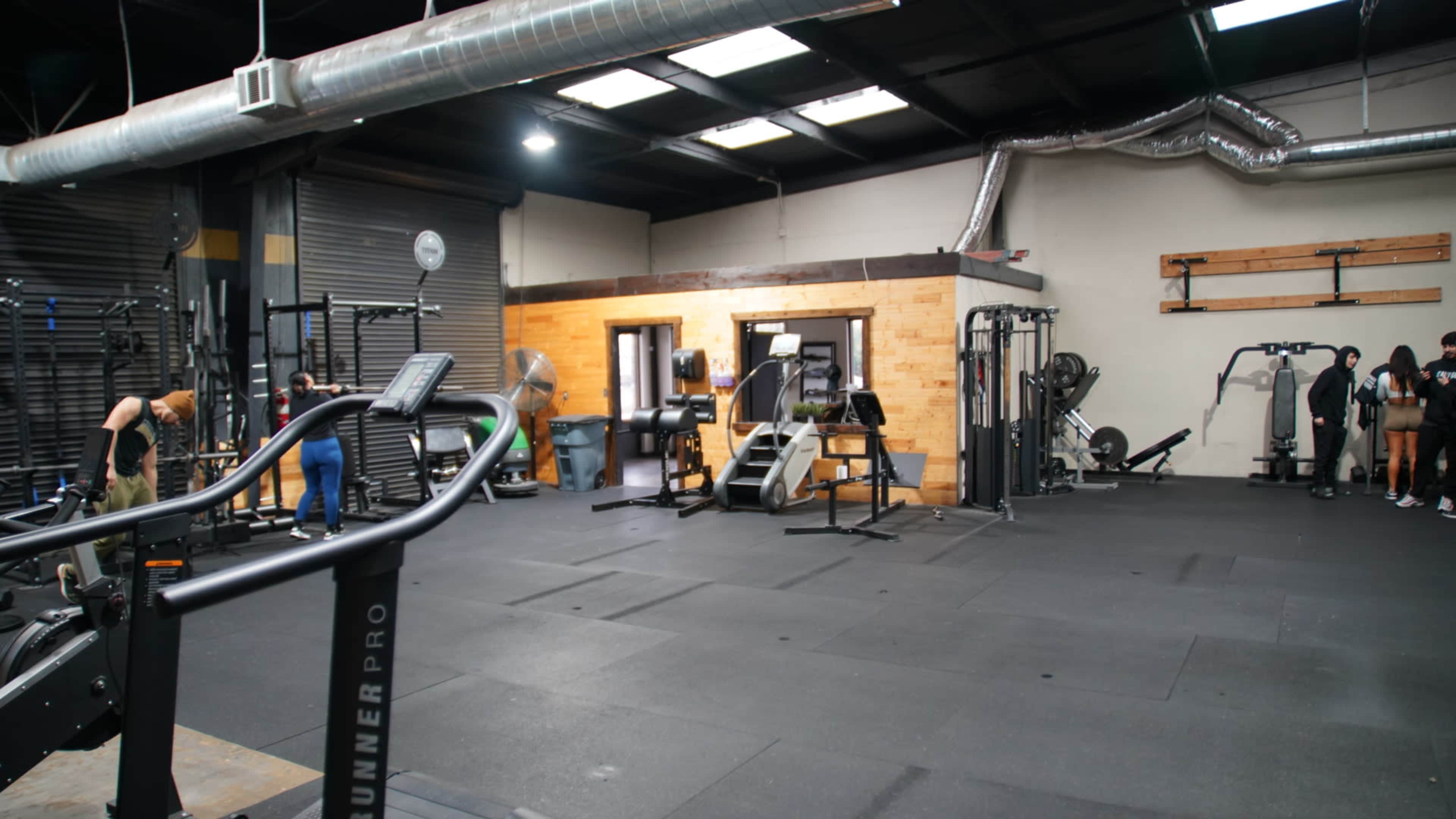 A gym interior with various exercise equipment and individuals working out in a spacious area.
