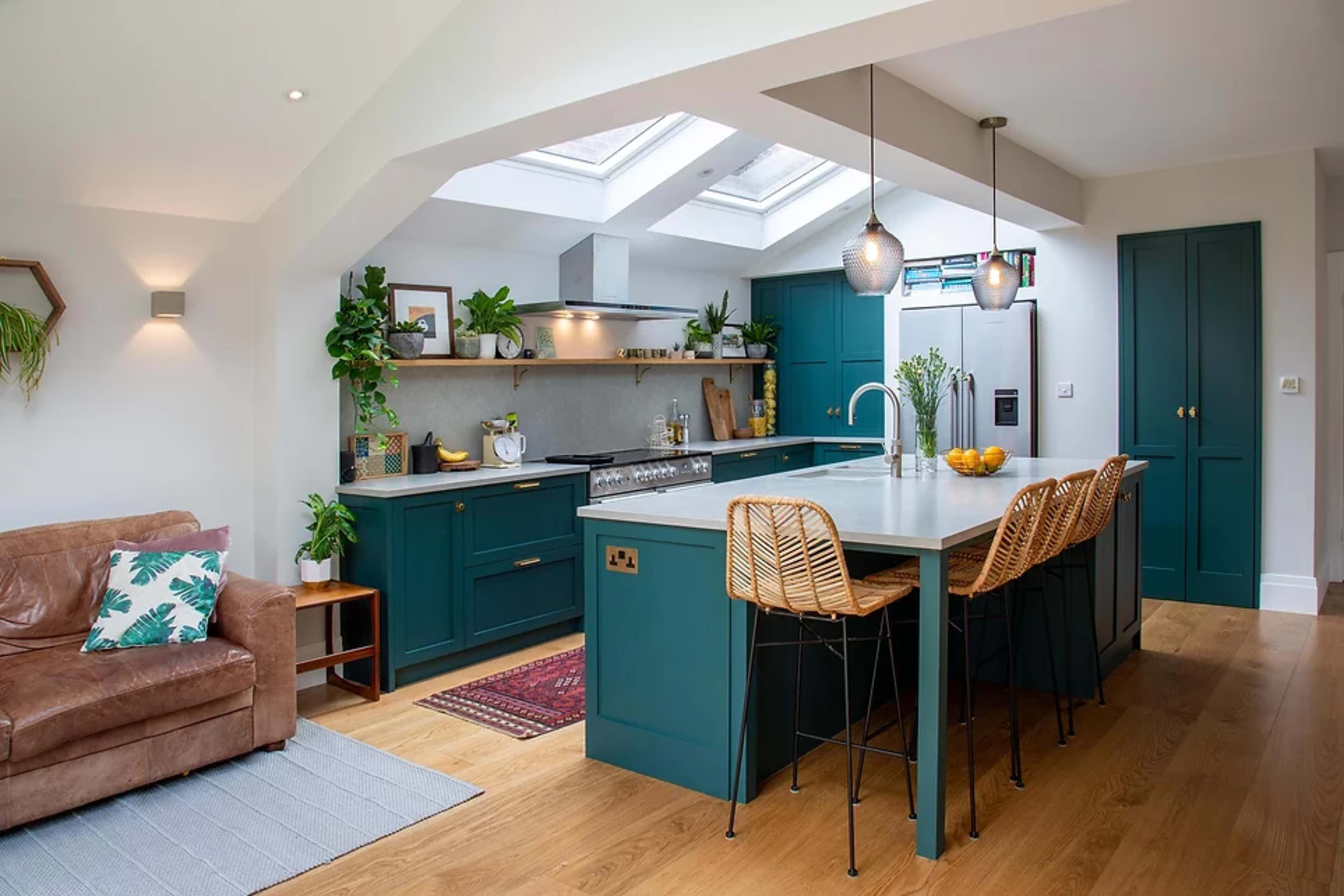 A modern kitchen with teal cabinetry, a large island with bar stools, and skylights that provide natural light.
