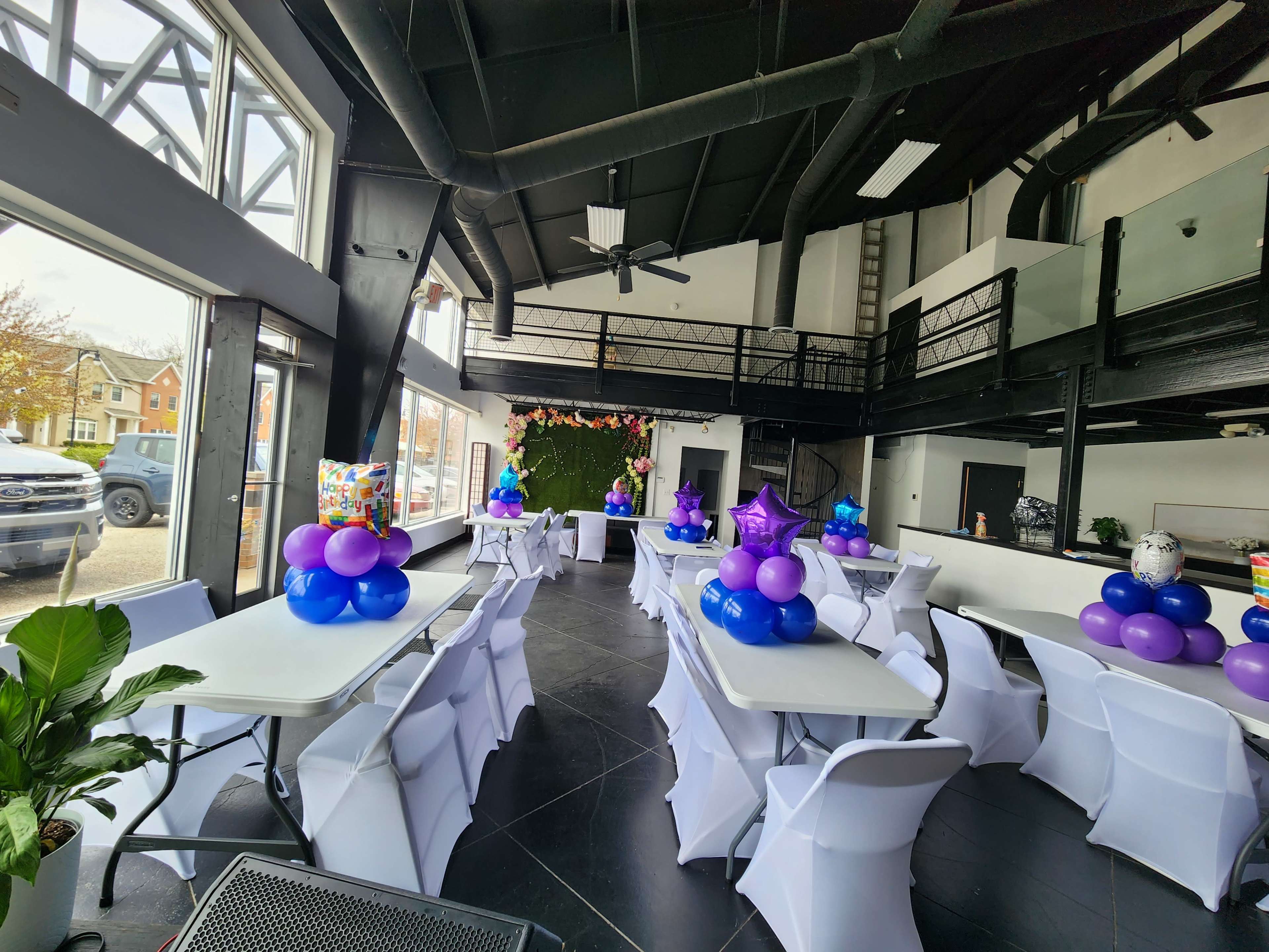 A modern event space with white tables decorated with blue and purple balloons, arranged for a gathering.