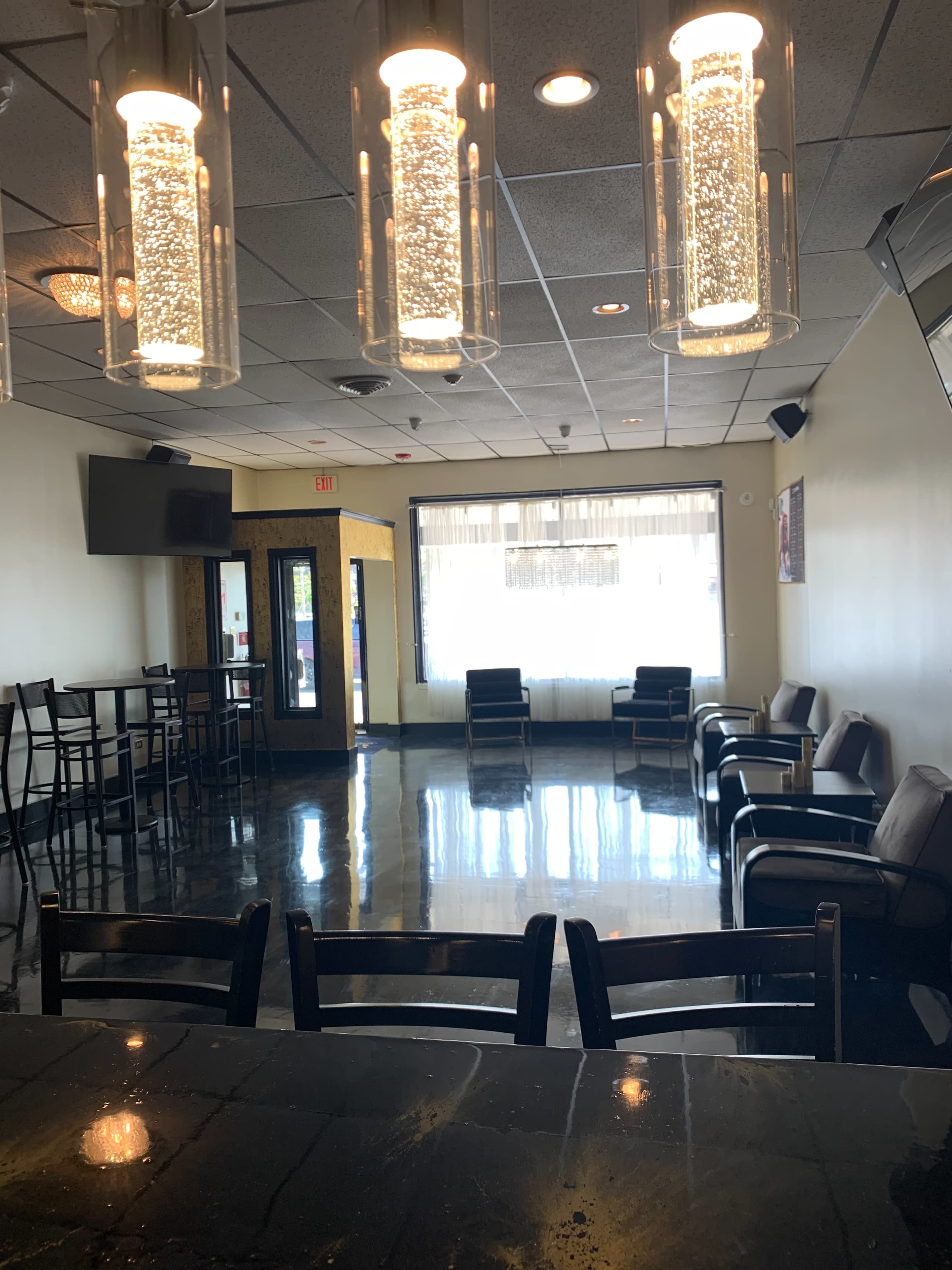 A modern lounge area with black tile flooring, illuminated pendant lights, and several black chairs arranged around tables.