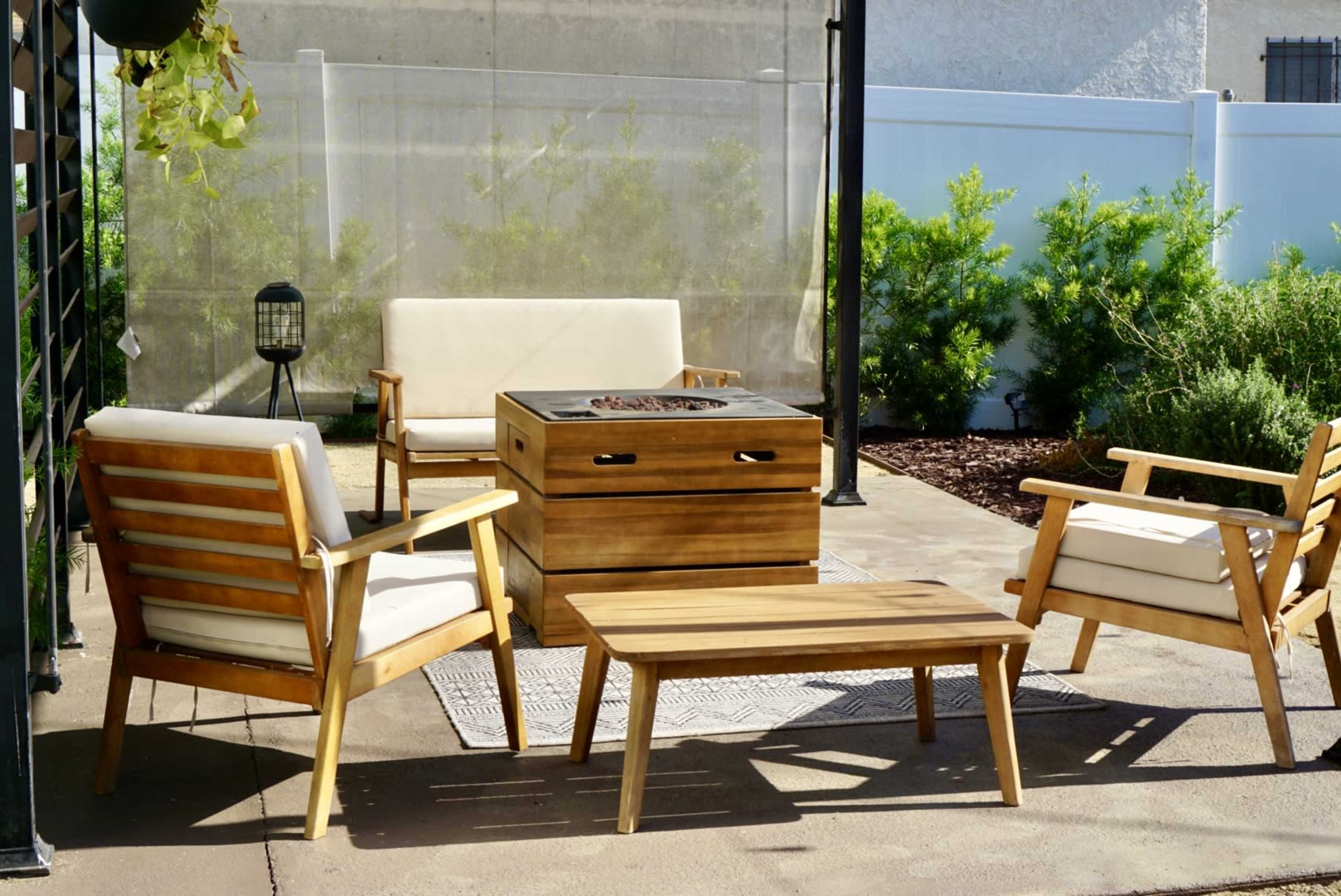 A patio seating area features wooden chairs and a table surrounding a fire pit on a concrete surface.