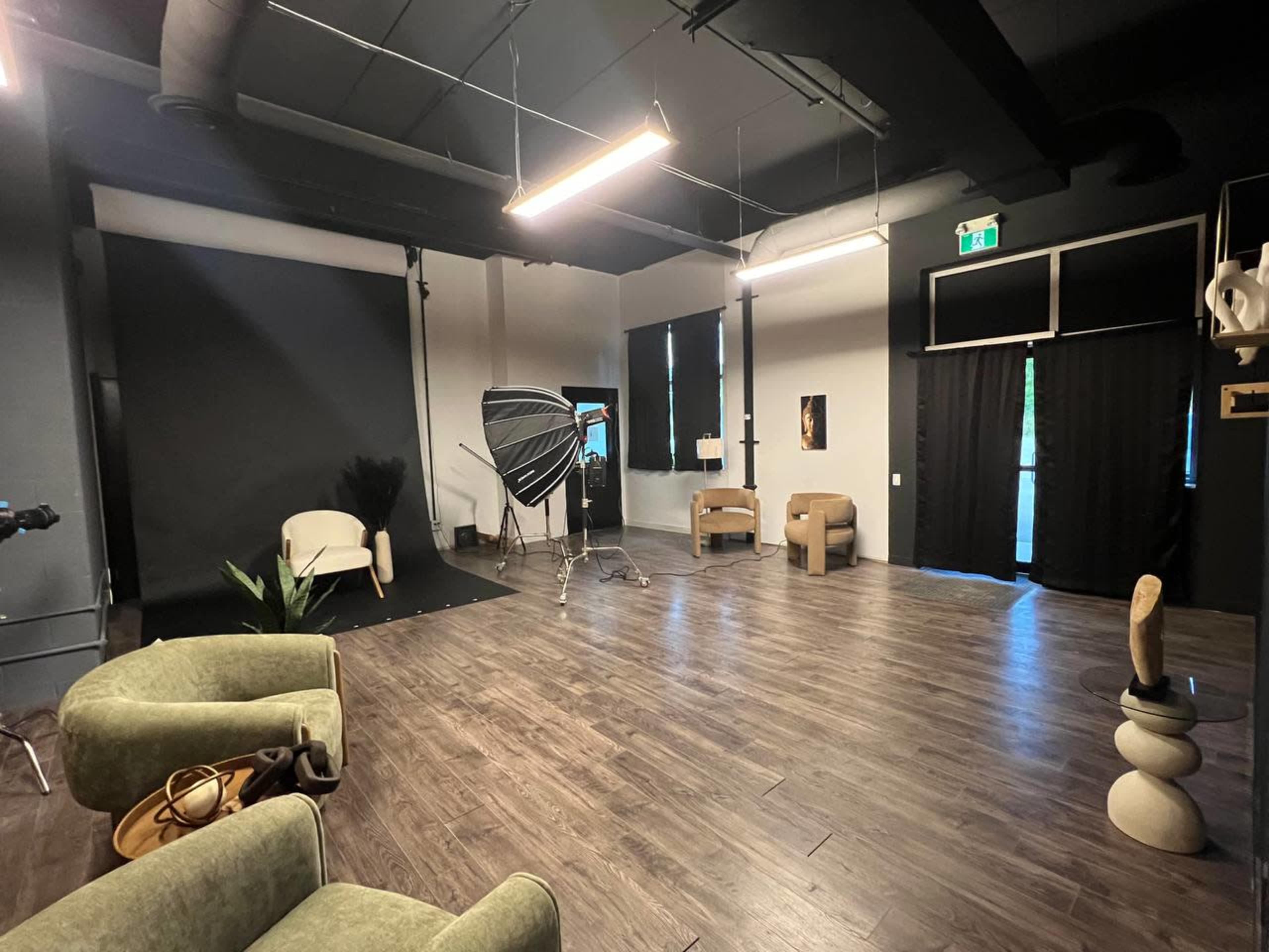The image shows a spacious photography studio featuring a black backdrop, lighting equipment, and several seating arrangements.
