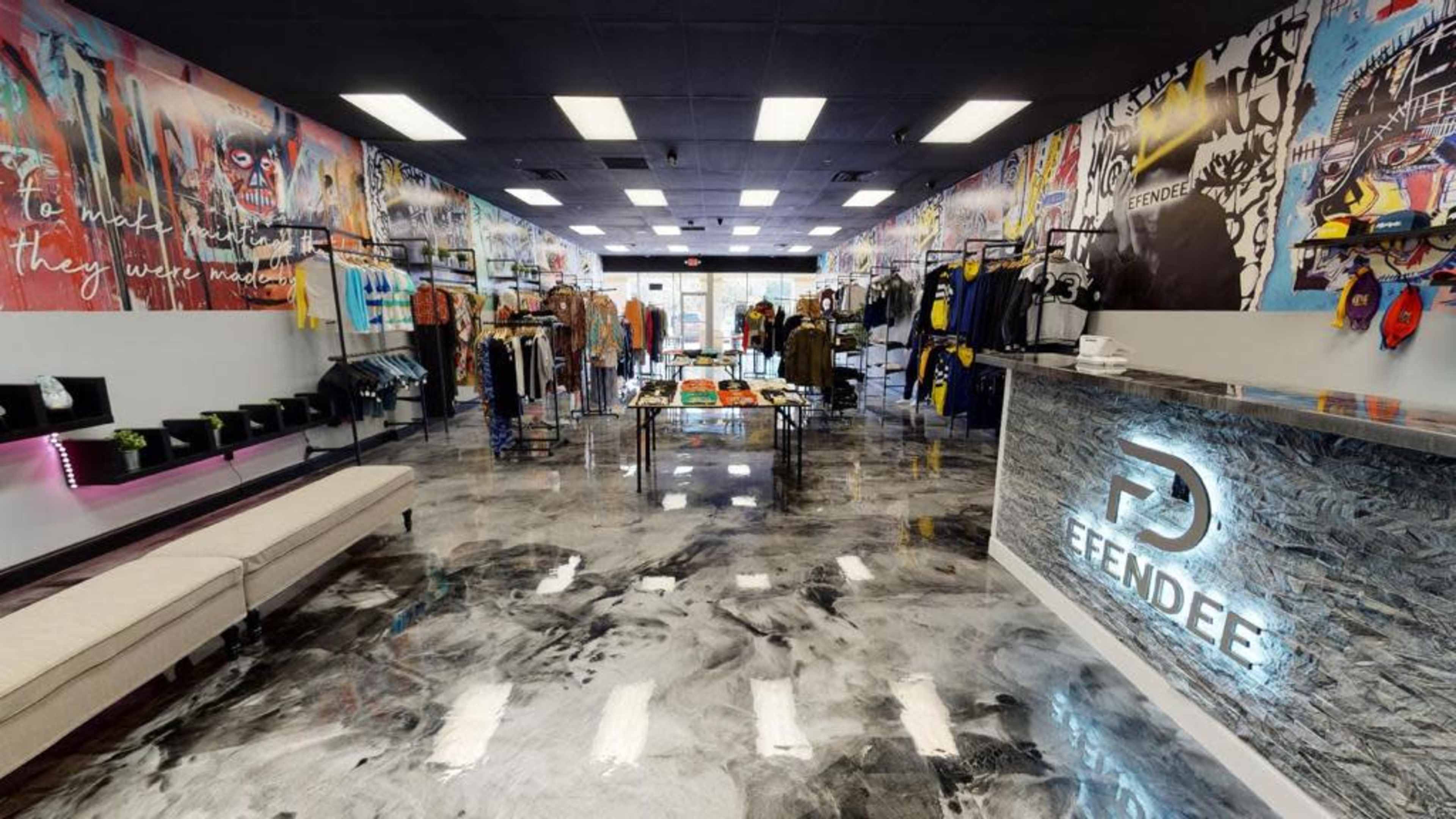The image shows a modern retail store featuring colorful graffiti-style artwork on the walls, clothing displays on racks, and a reception area with a branded counter.