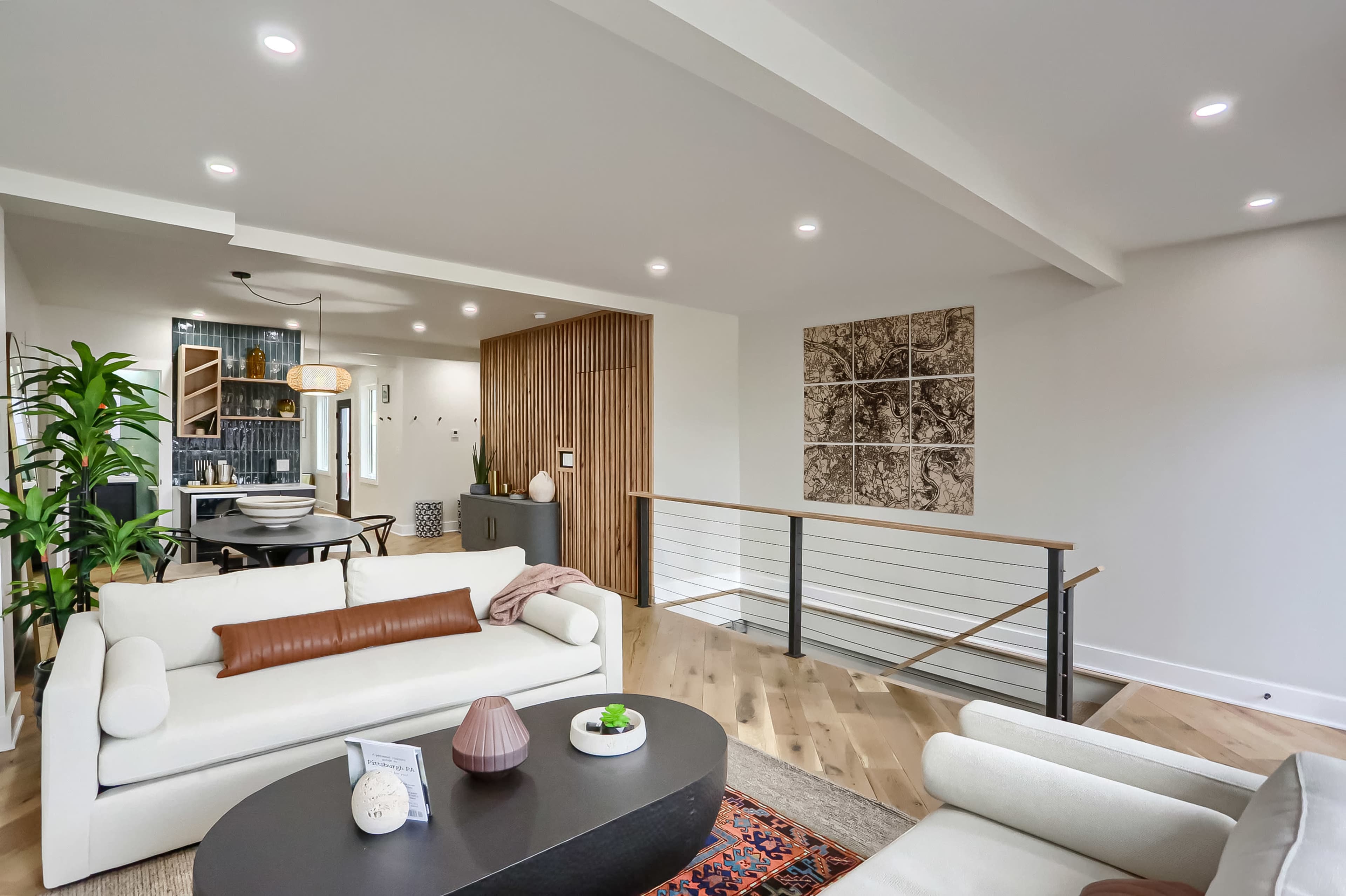 The image shows a modern living room with two light-colored sofas, a coffee table, and a view of a dining area featuring a round table and contemporary decor.