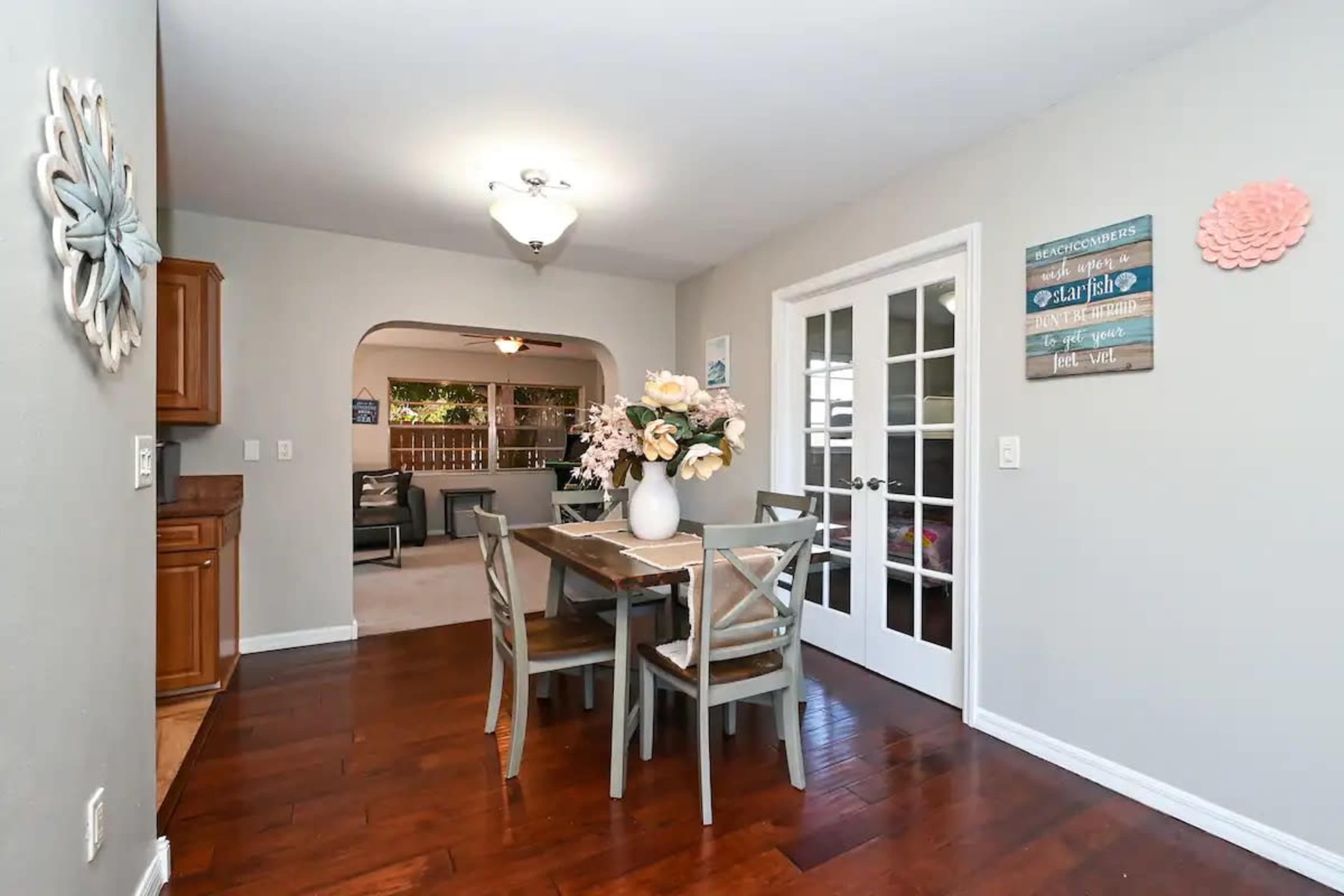 A dining area features a wooden table with chairs, a floral centerpiece, and a doorway leading to another room.