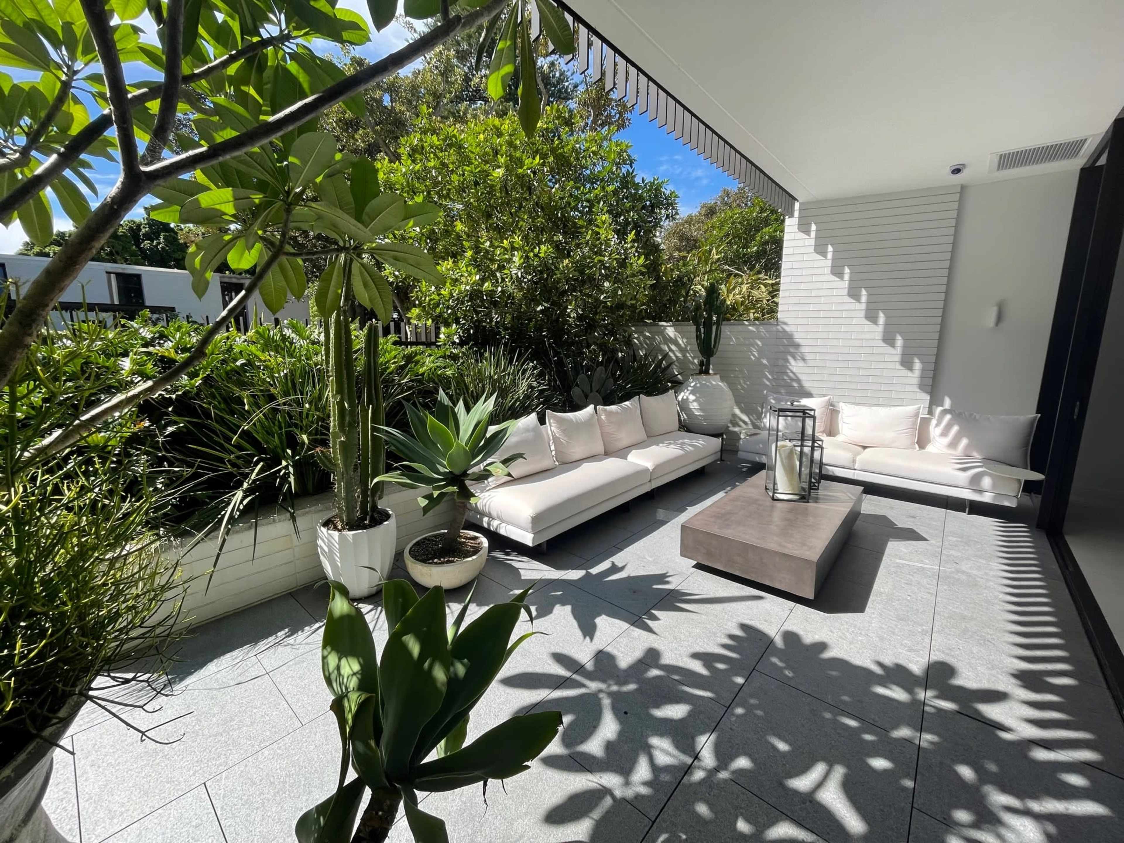 A modern outdoor seating area features a light-colored sofa, a coffee table, and lush greenery in planters.