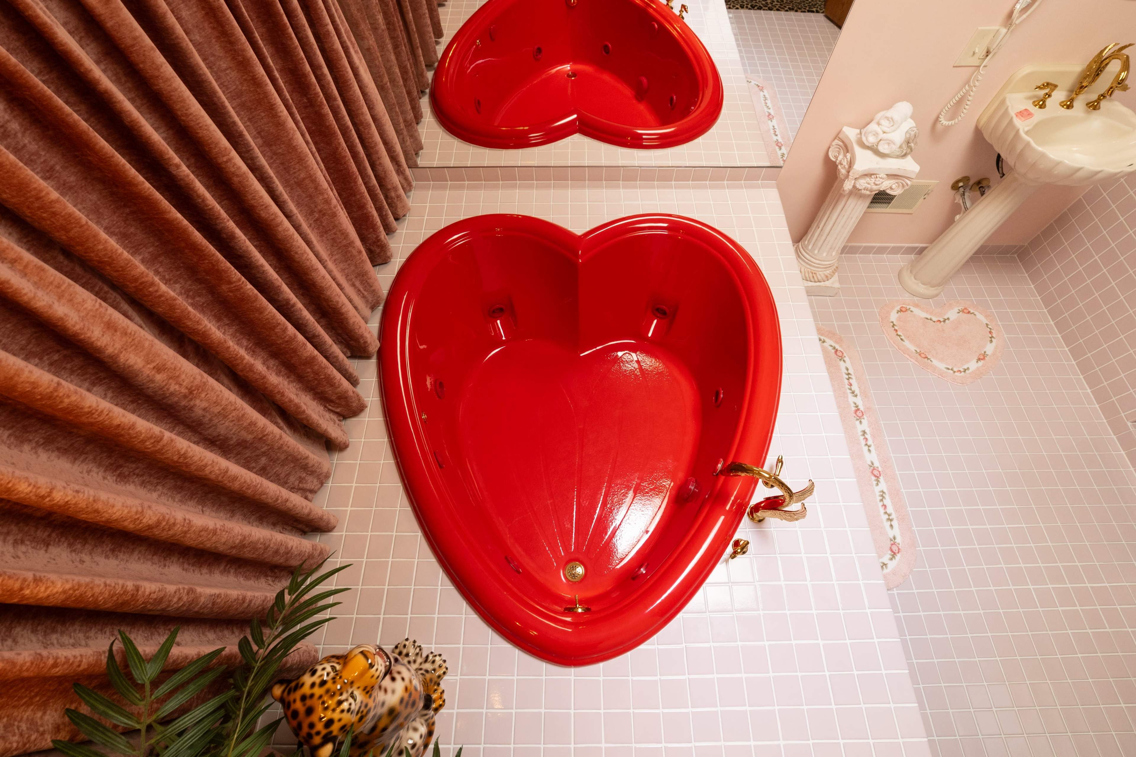 The image shows two red heart-shaped bathtubs positioned in a pink-tiled bathroom.
