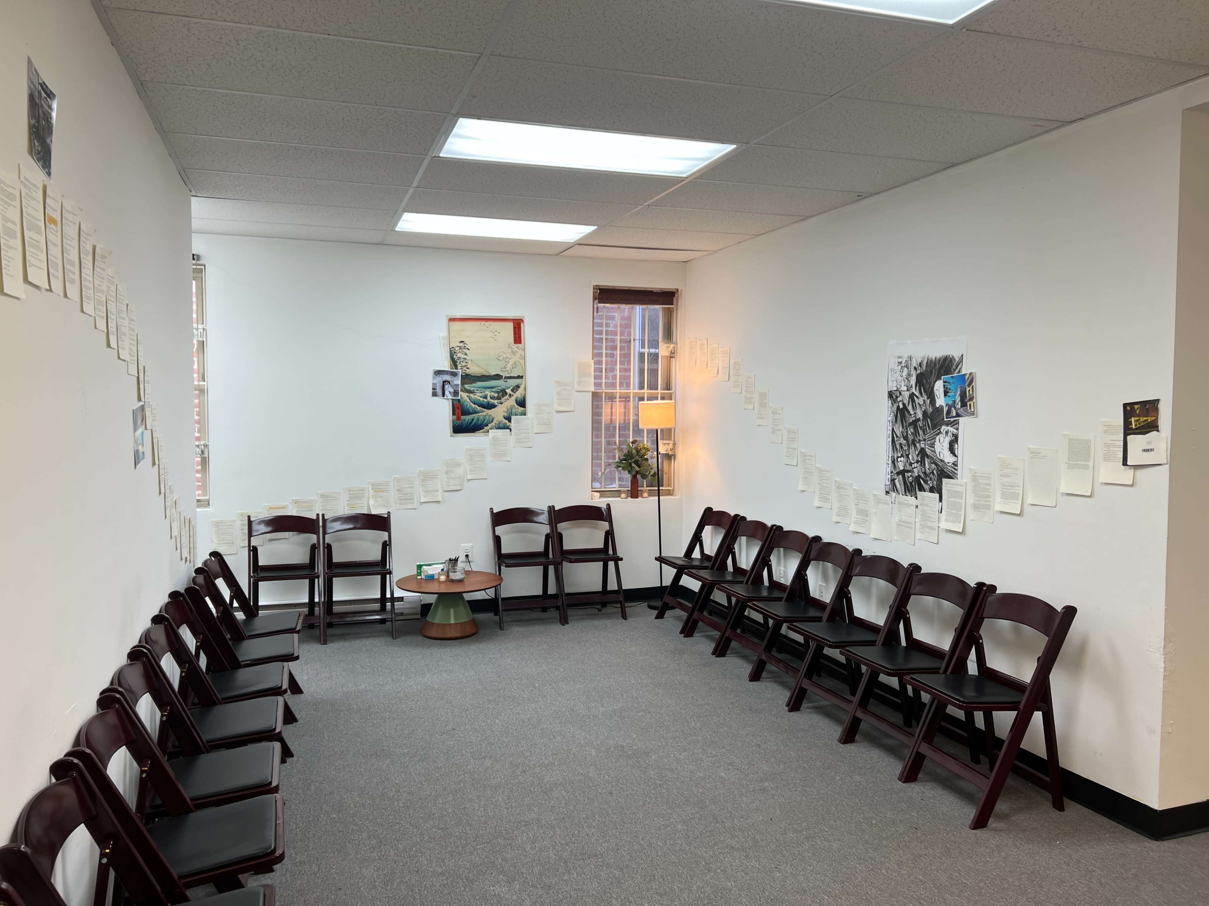 A waiting area features a circle of chairs with pages of text arranged along the walls and a small table in the center.