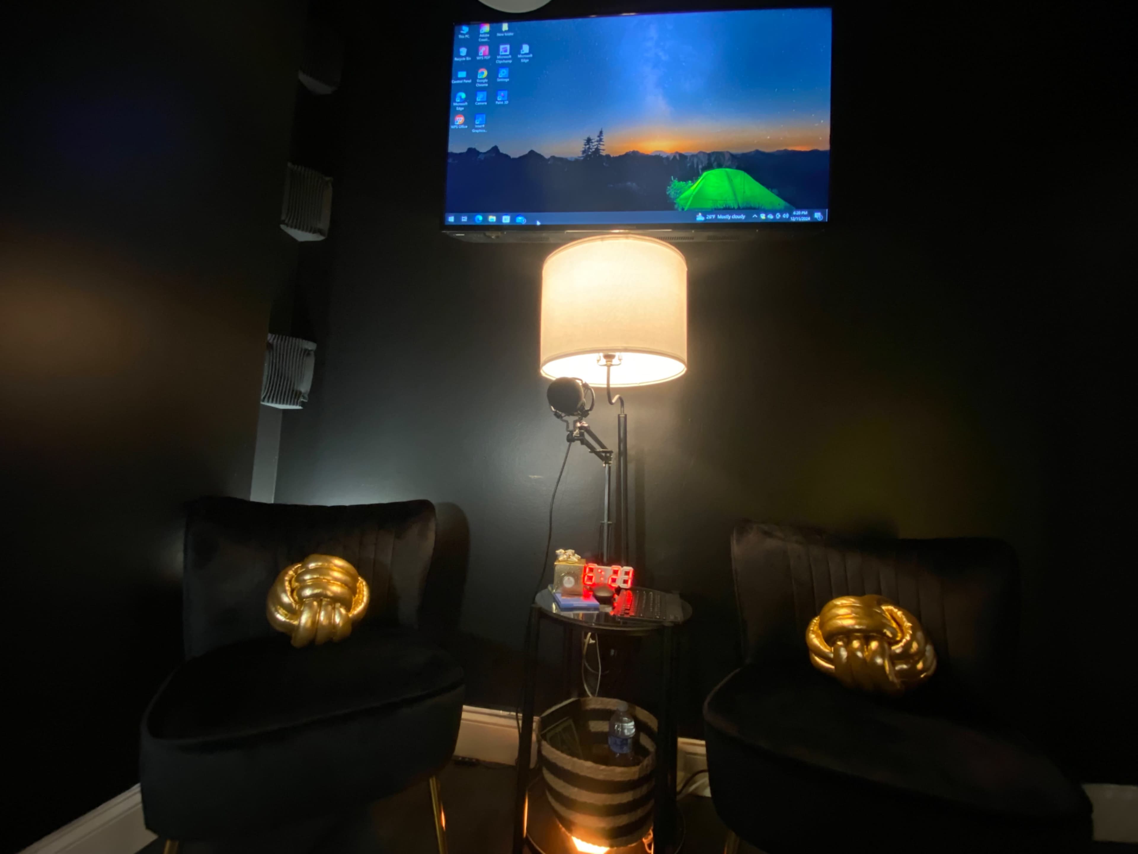 The image shows a small room with two black velvet chairs, a floor lamp, and a wall-mounted TV displaying a landscape background.