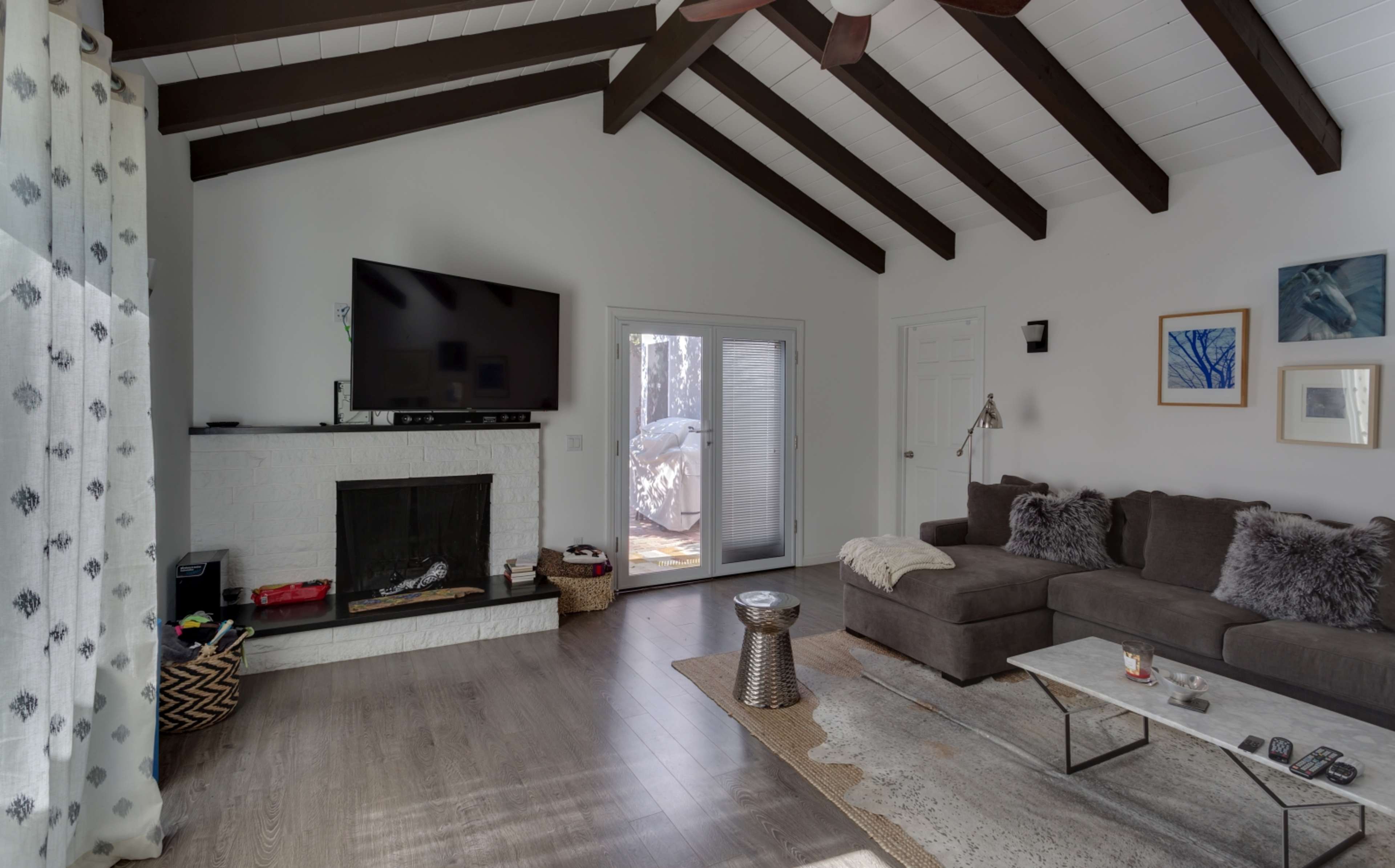 The living room features a sectional sofa, a flat-screen TV mounted above a white fireplace, and large windows with natural light streaming in.