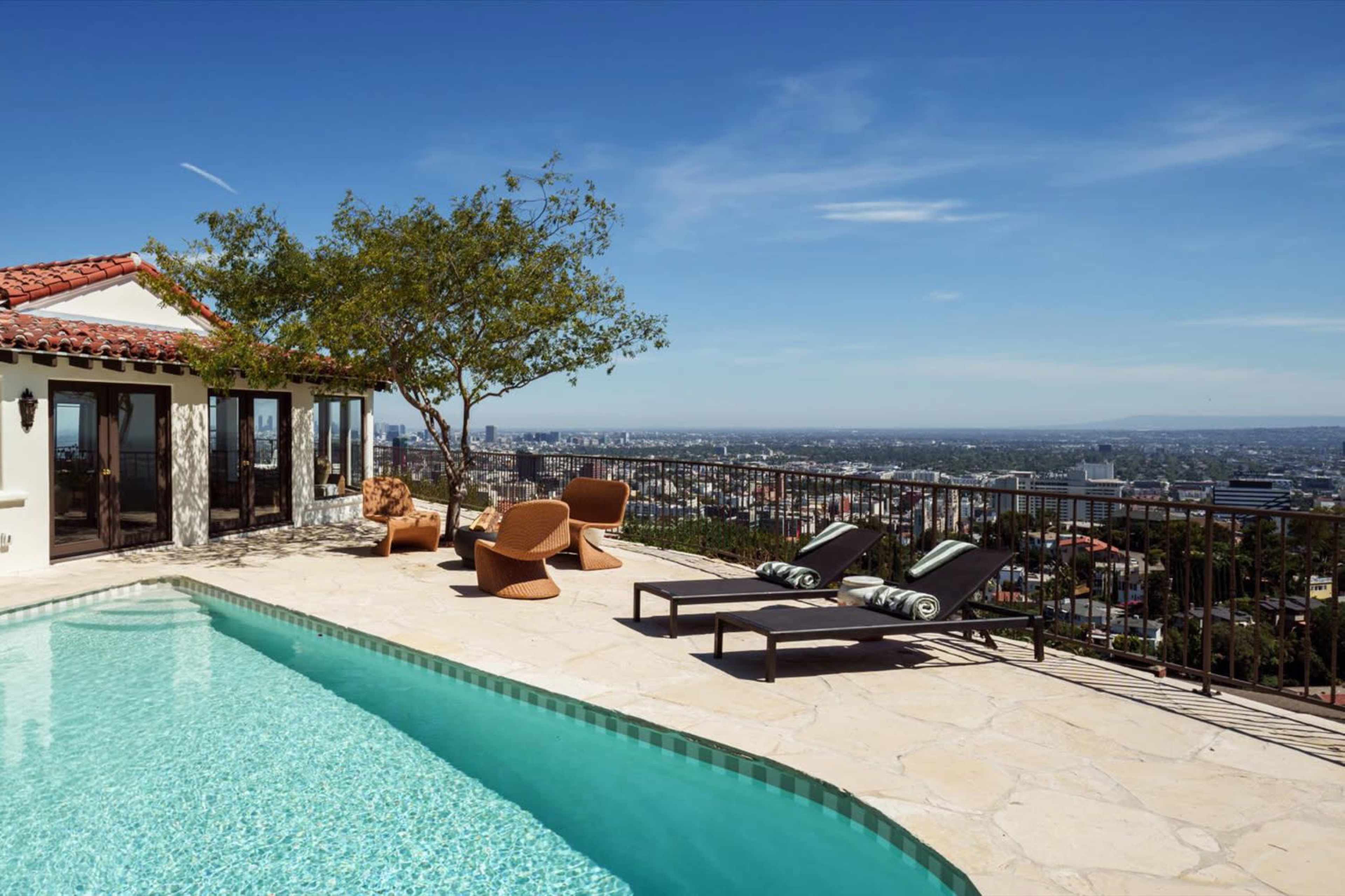 A swimming pool with lounge chairs overlooks a cityscape from a hillside patio.