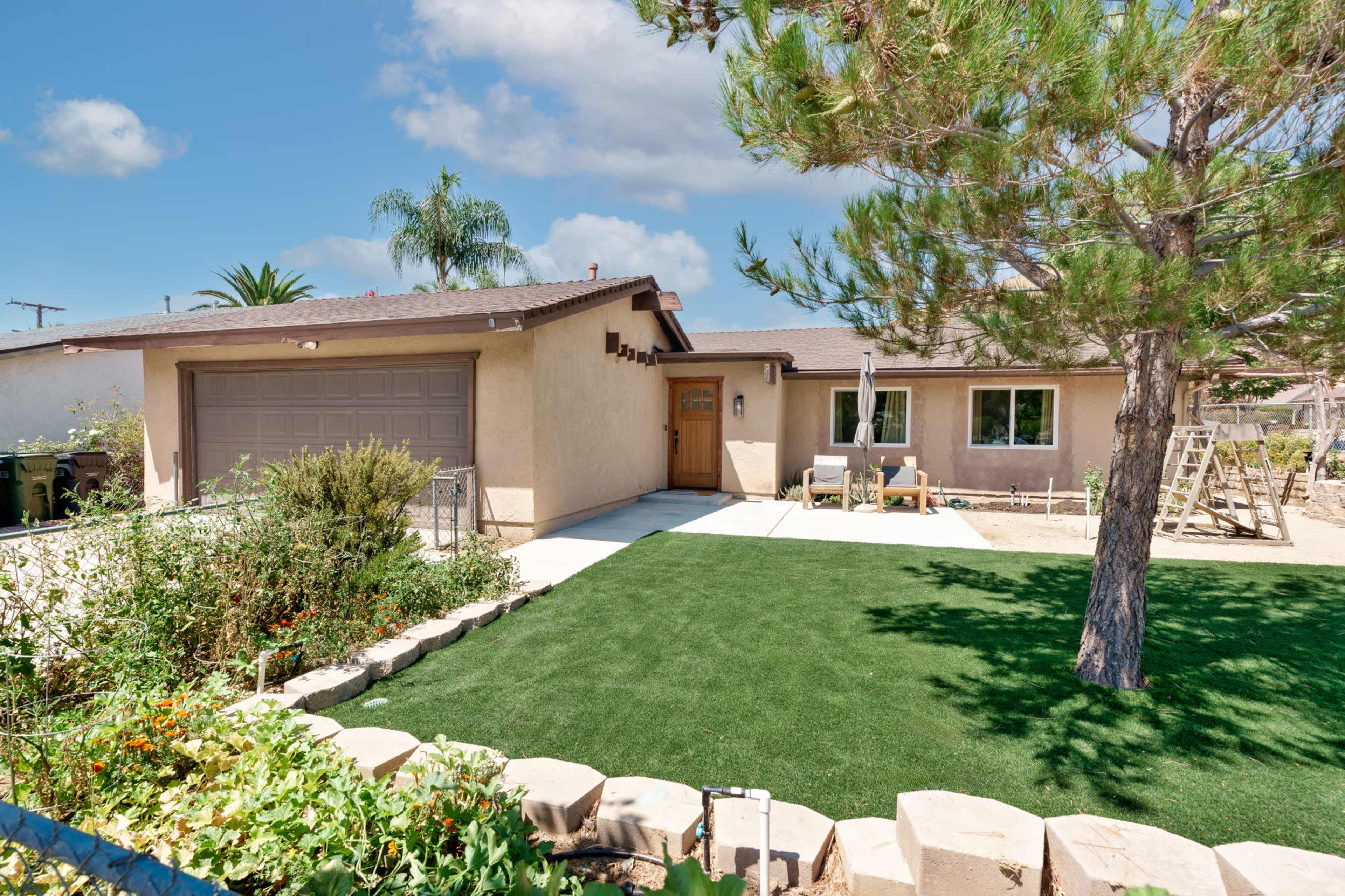 The image shows a single-story house with a garage, a green lawn, and a tree in the front yard.